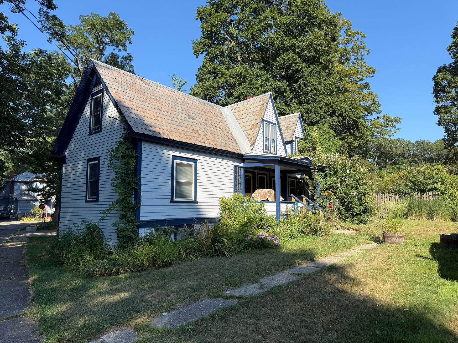 Blue and white house with a porch, surrounded by greenery under a blue sky.