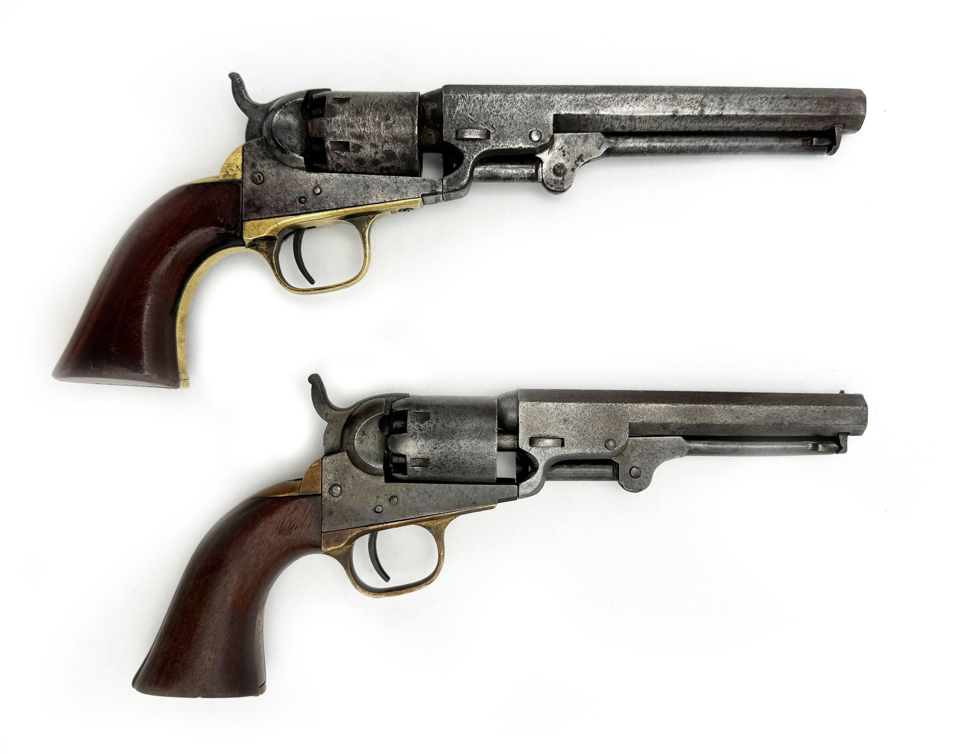 Two antique Colt revolvers with wooden grips and metal frames on a white background.