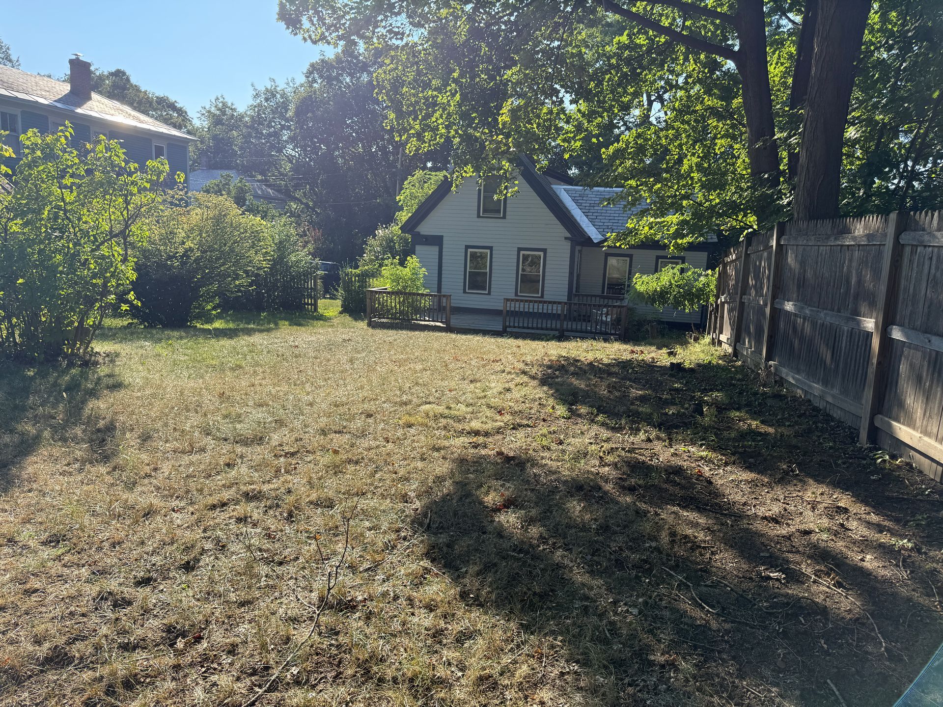 A small house with a yard on a sunny day. A wooden fence is on the right.