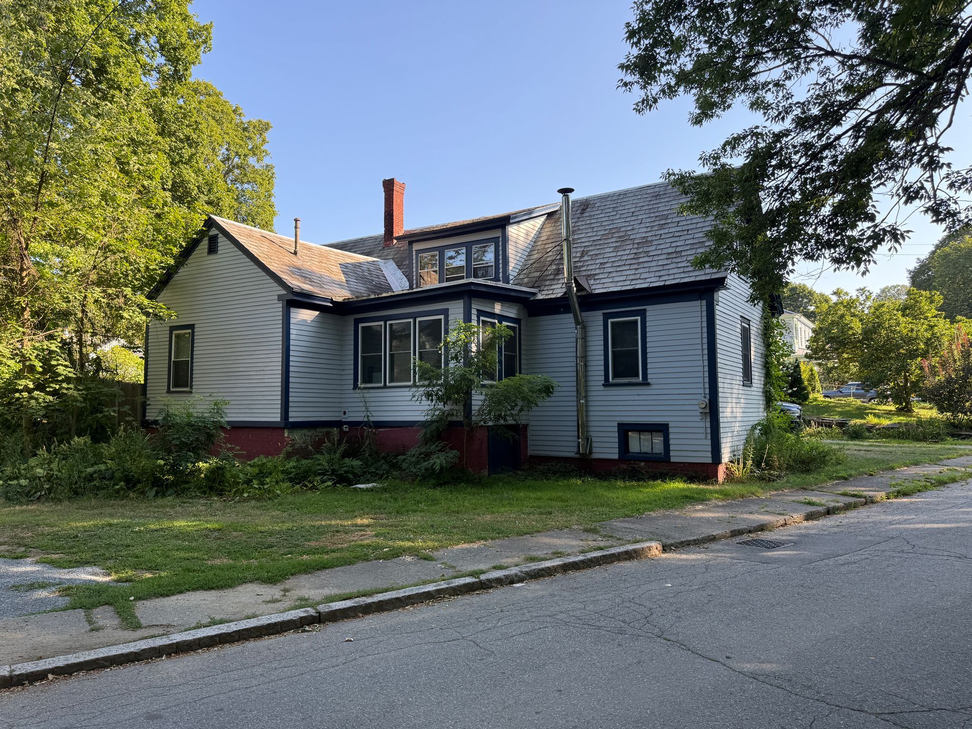A two-story, light-blue house with yard, visible from a gray street, under a sunny sky.