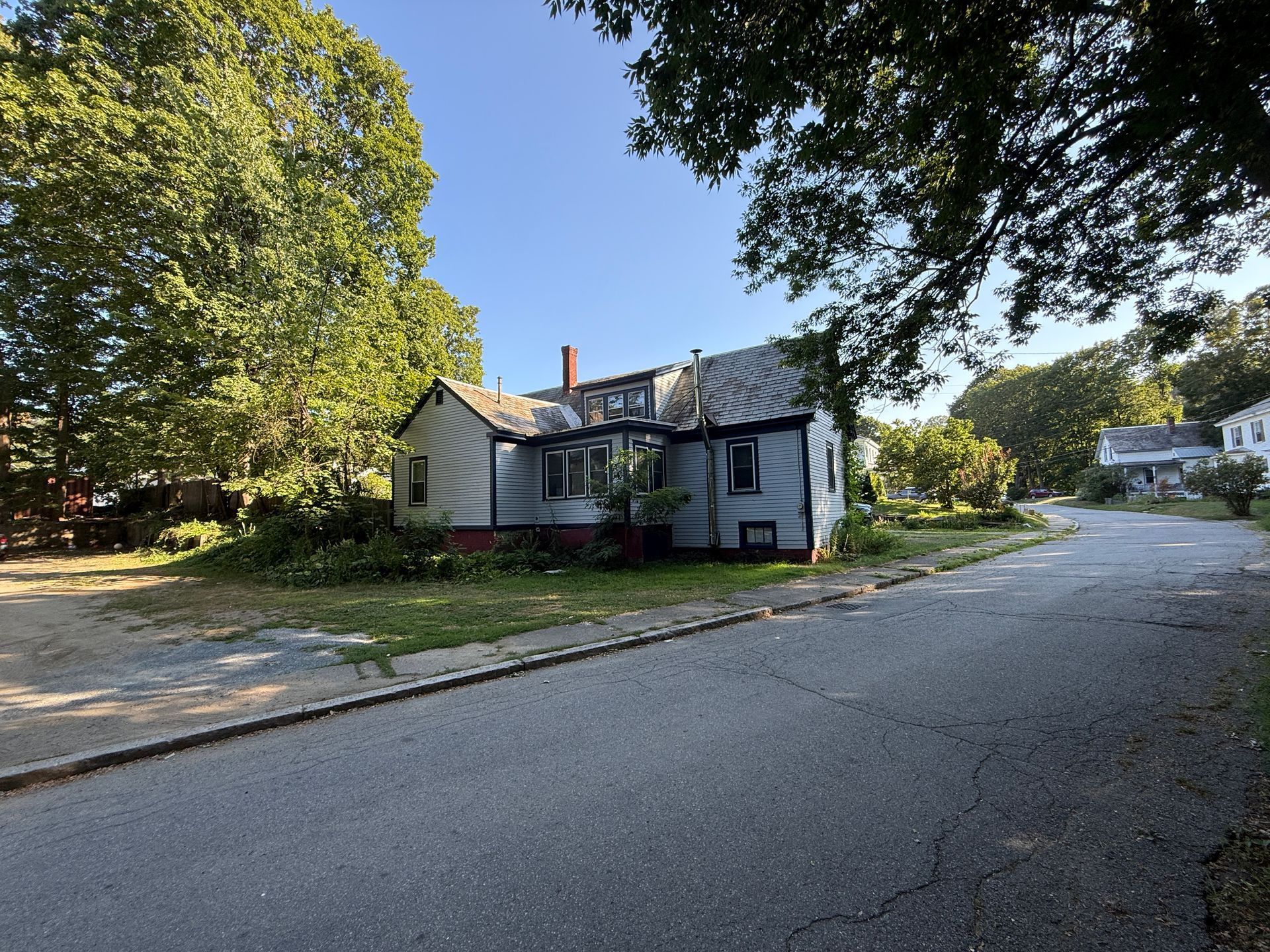 Gray house on a street, trees on either side, overcast sky.