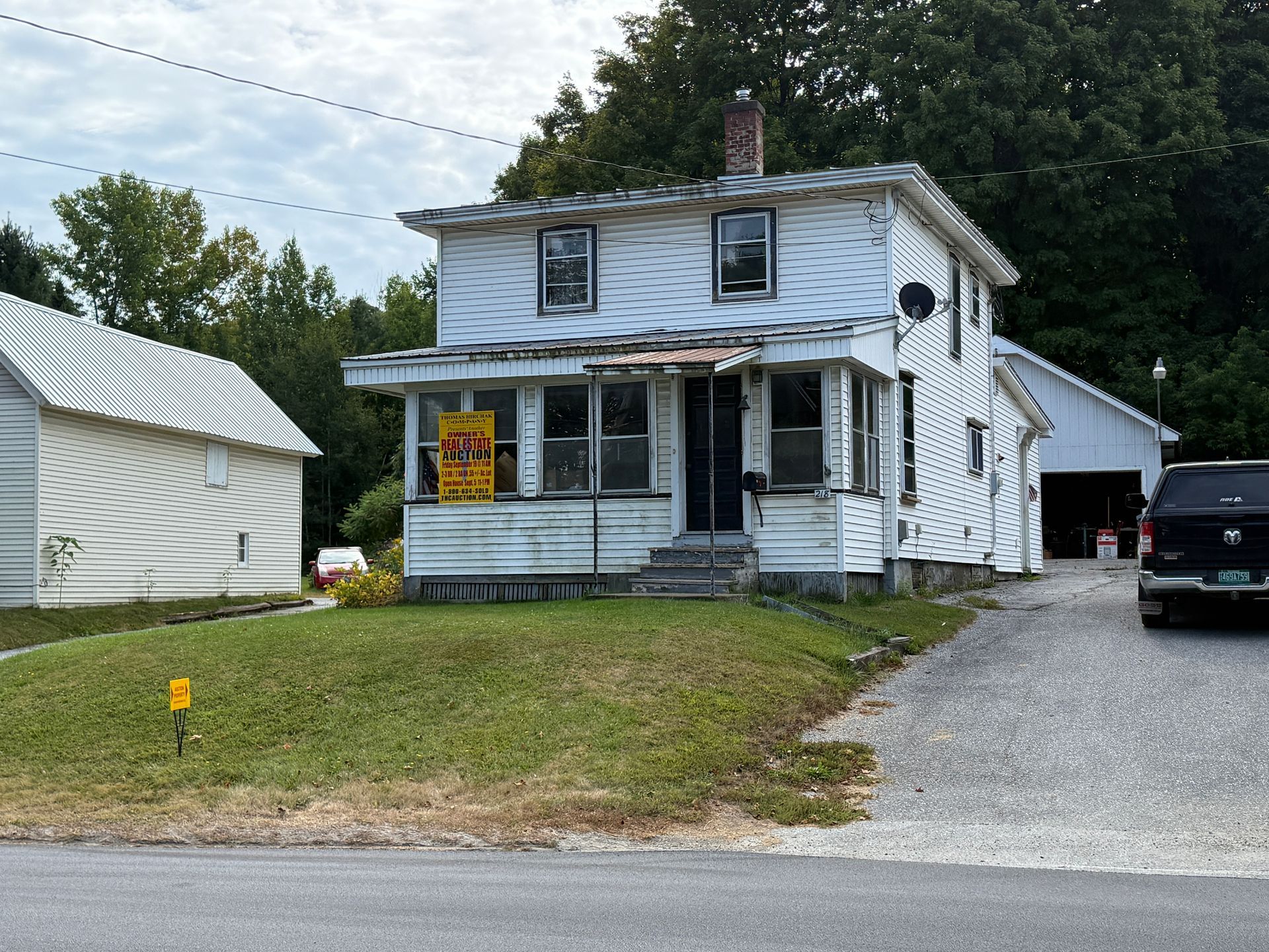 White, two-story house with a porch and a small yard. A sign hangs on the porch.
