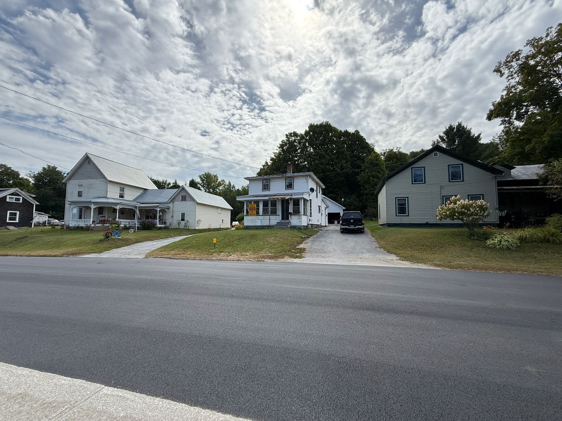 Several white houses along a paved road under a cloudy sky.