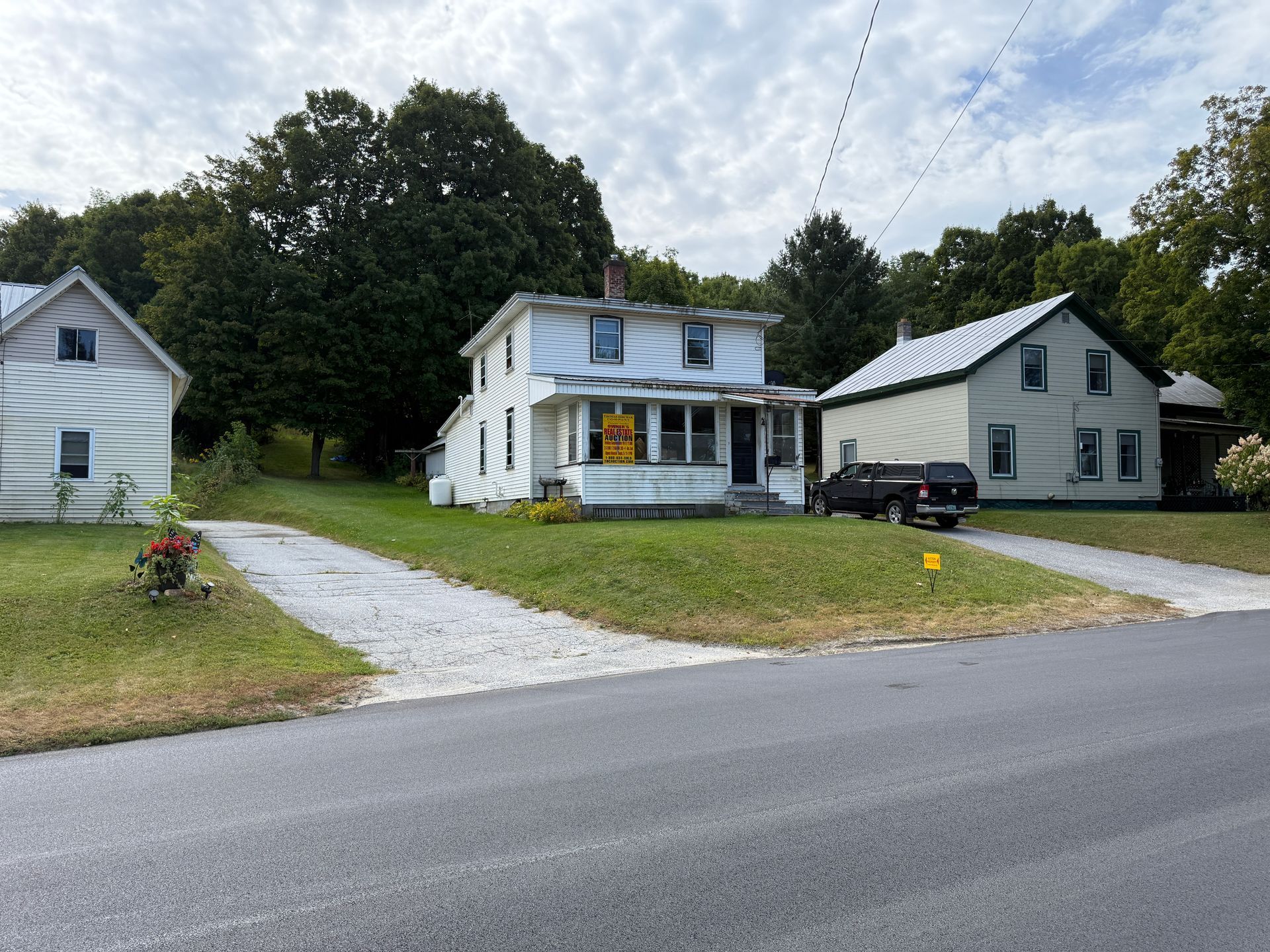 White house with driveway along a street. Green grass and trees are in the background.