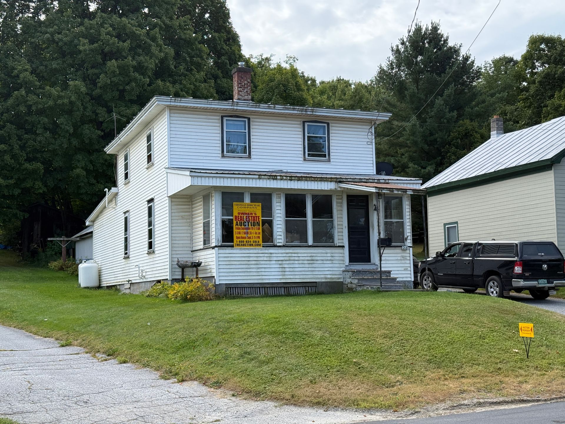 Two-story white house with porch and for sale sign on a grassy lot.
