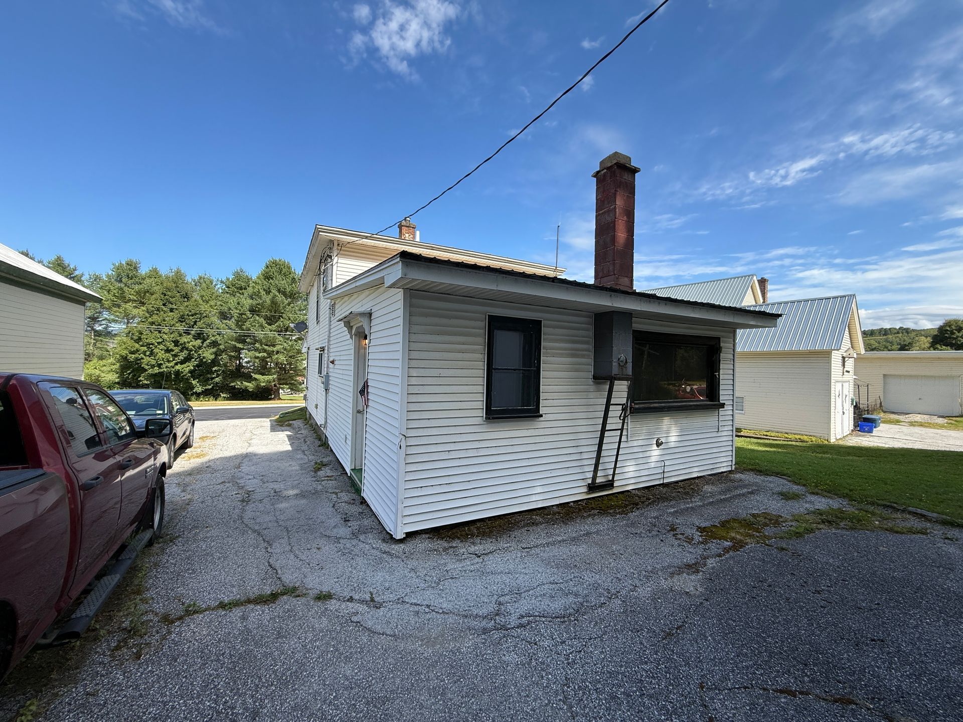 White weathered building with a red truck parked nearby on a gravel lot under a blue sky.