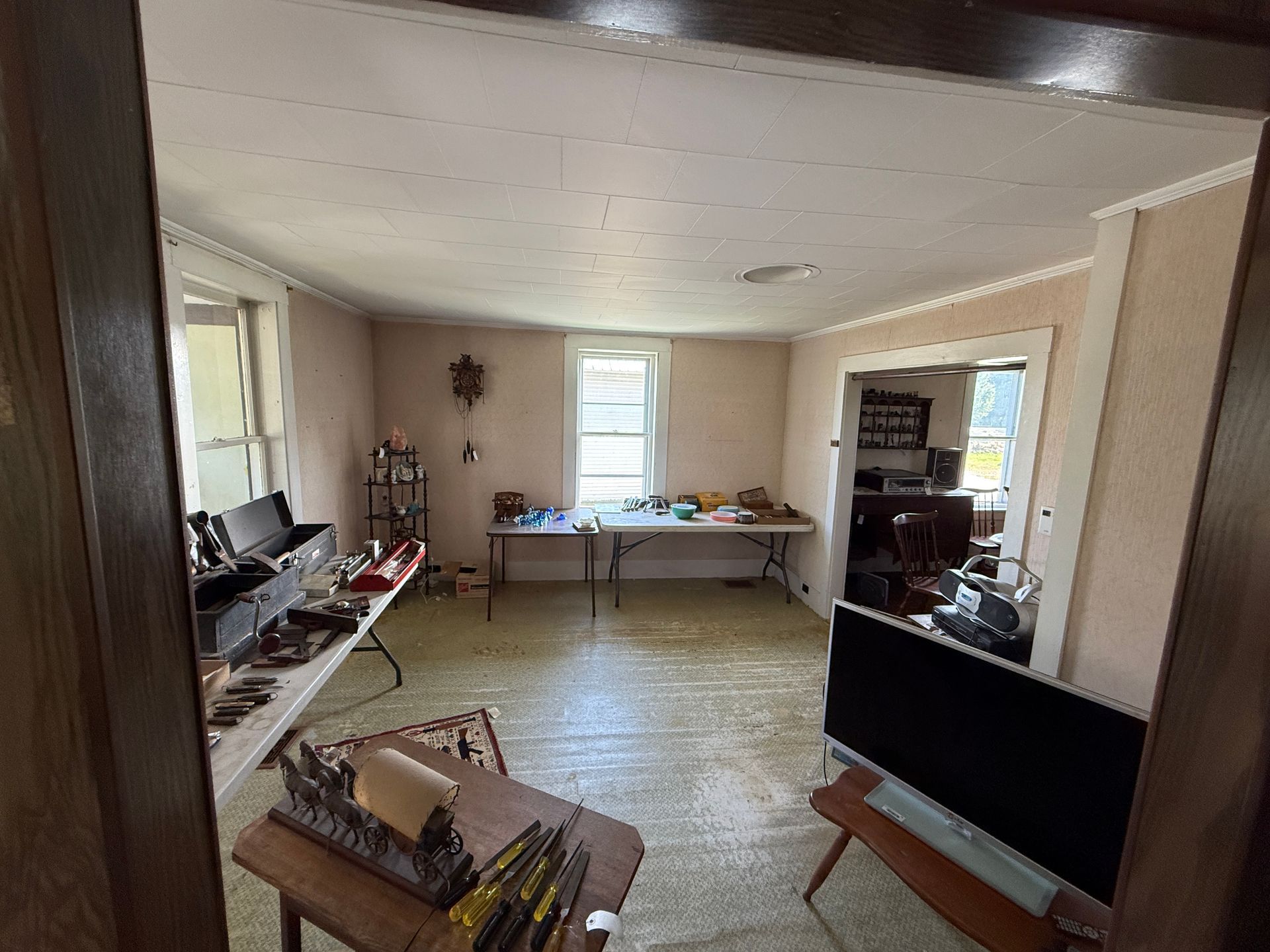 Room with tables displaying items. Open doorway to another room with more items and furniture.