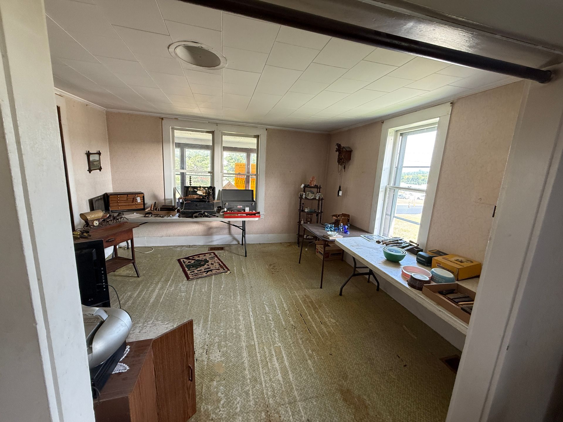 Room with windows and several tables laden with items; an open doorway is in the foreground.