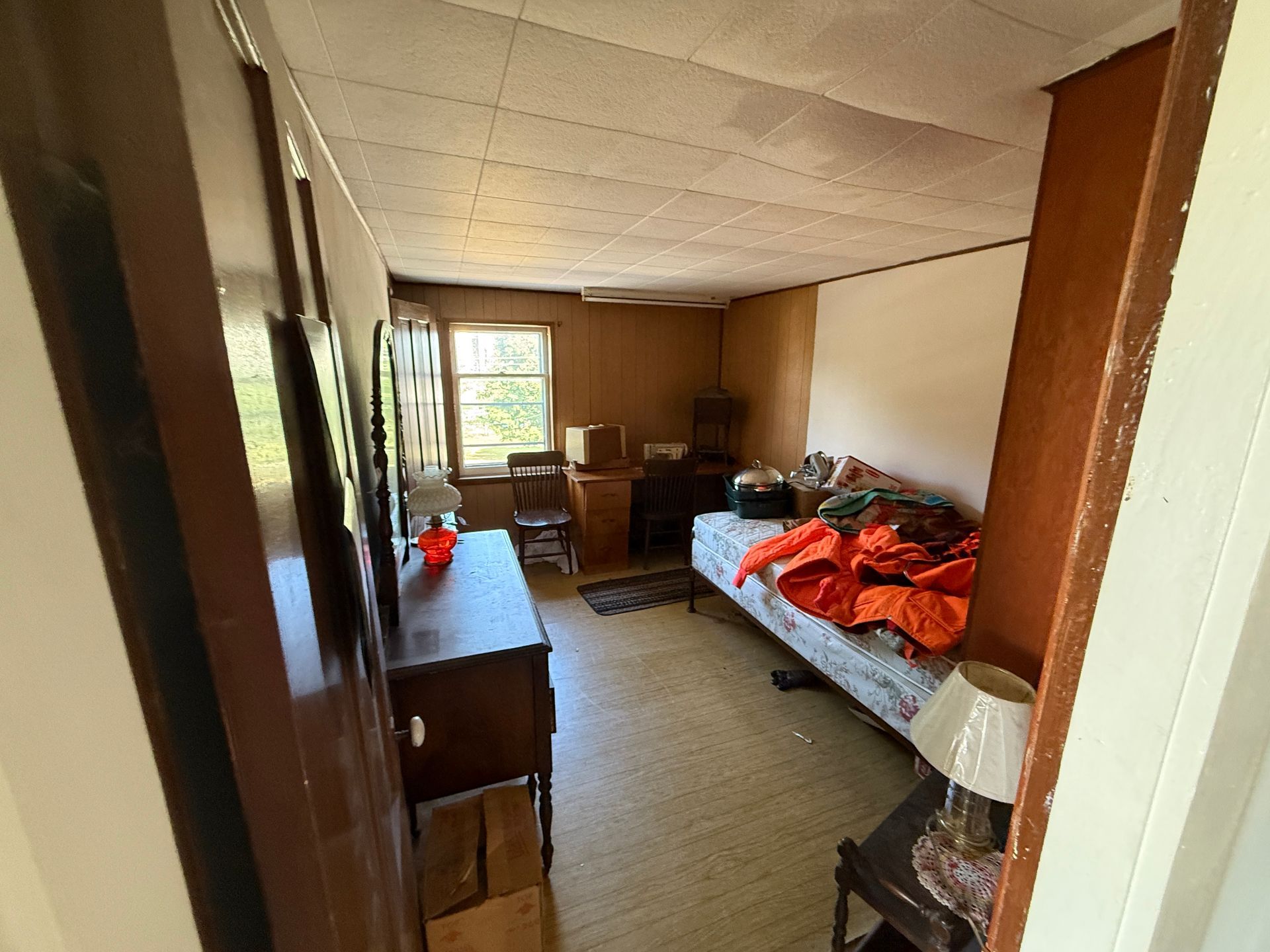 Interior view of a small room with a bed, dresser, desk, and window.