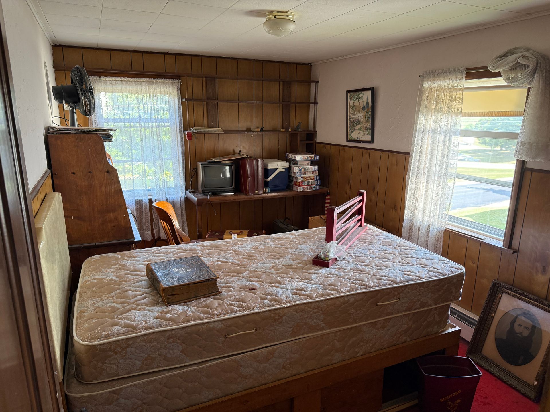 Bedroom with a mattress, wooden paneling, a small TV, and an open window.