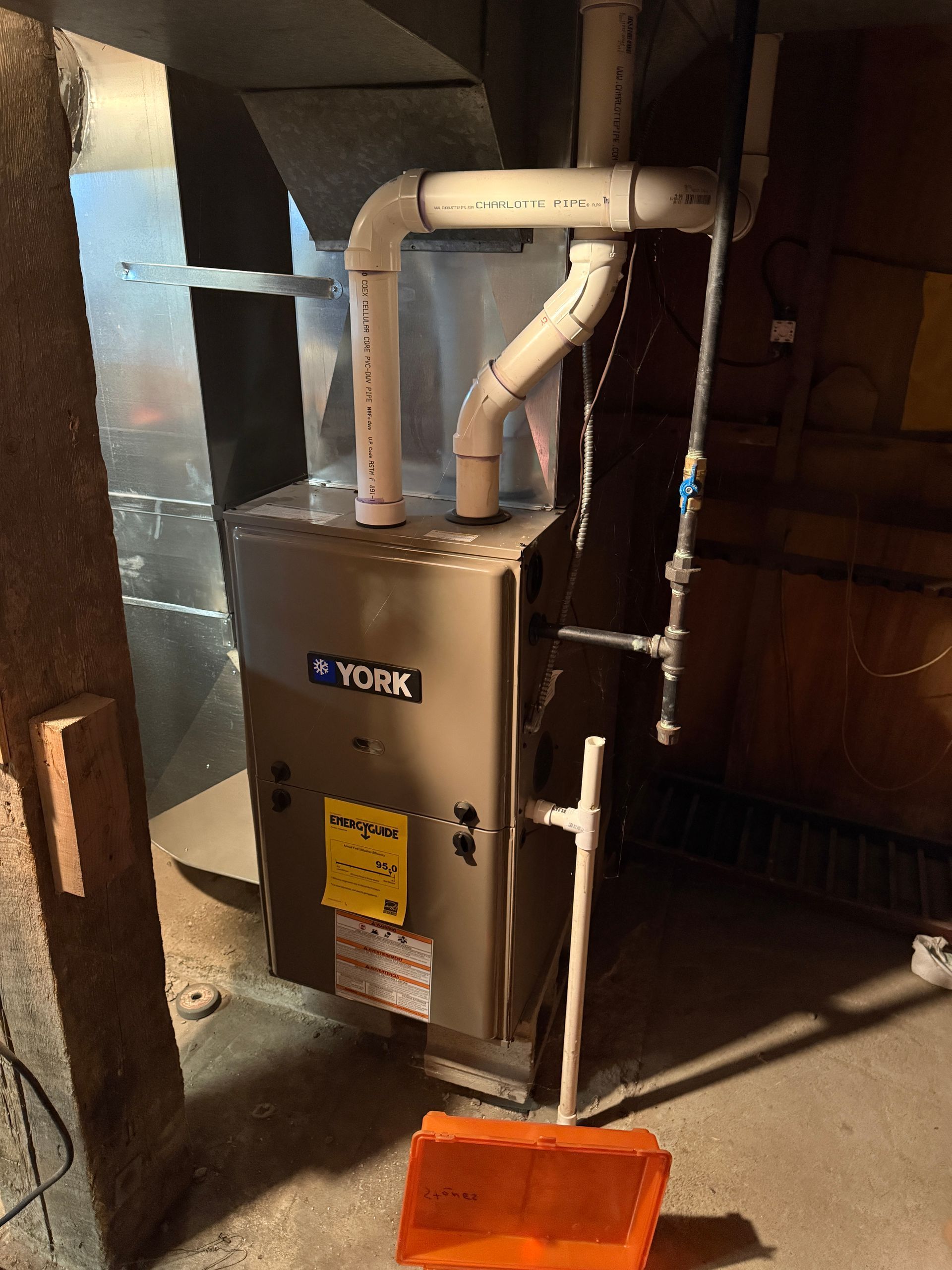 A York furnace in a basement setting with ductwork and PVC pipes, orange utility bucket in the foreground.