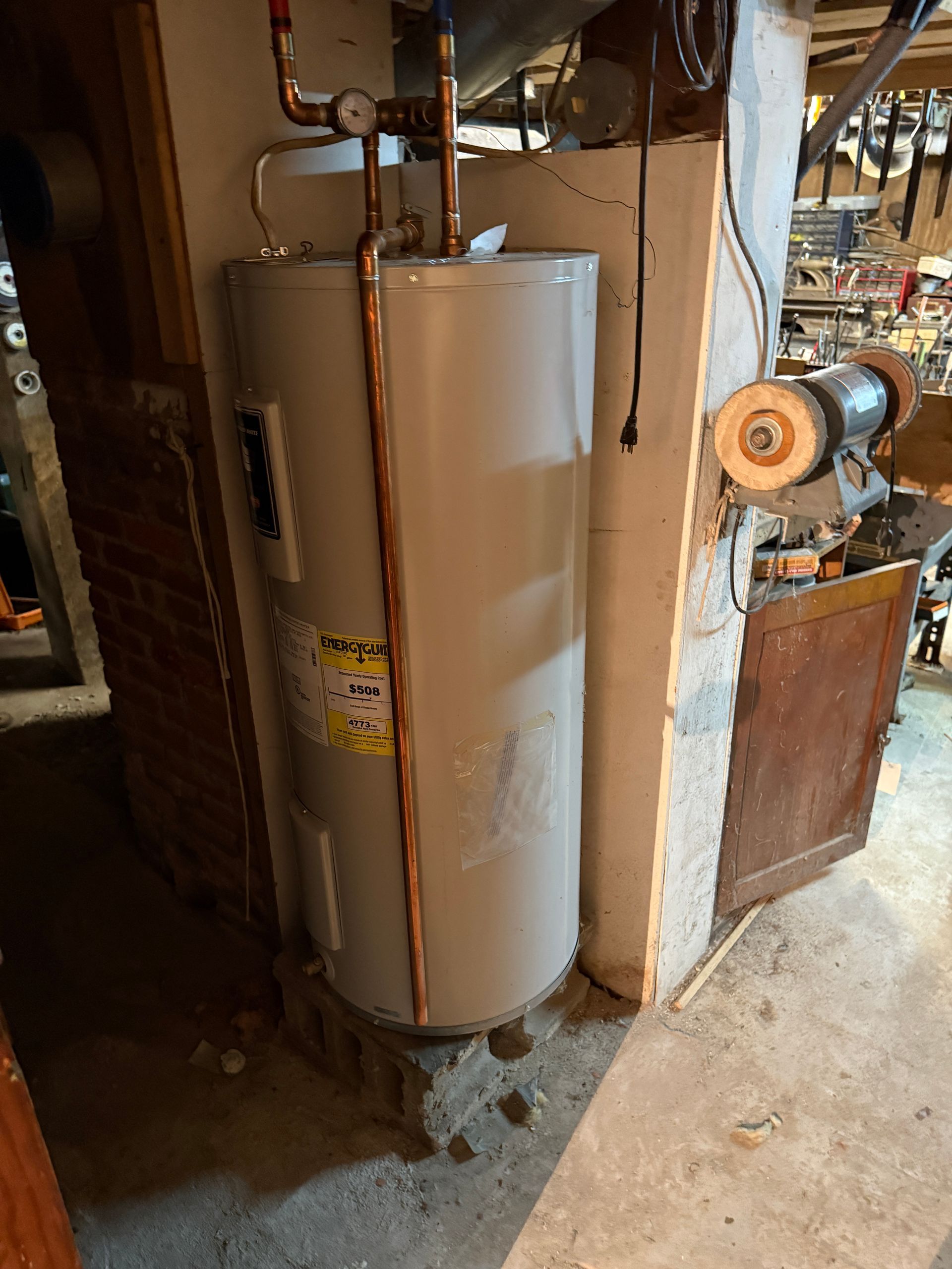Water heater in a basement. Copper pipes and yellow energy label are visible.