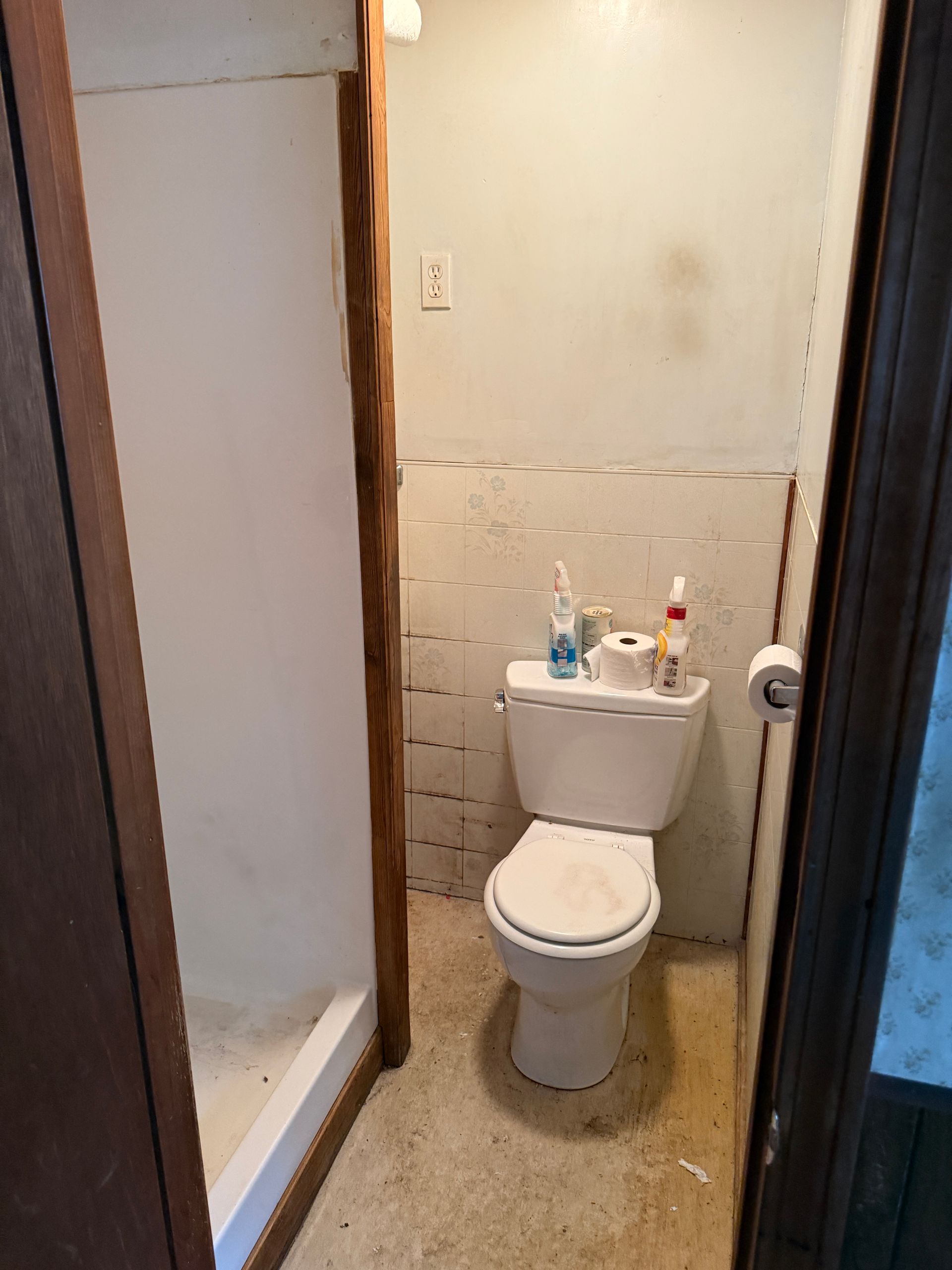 Small bathroom with toilet, shower stall, and stained walls.