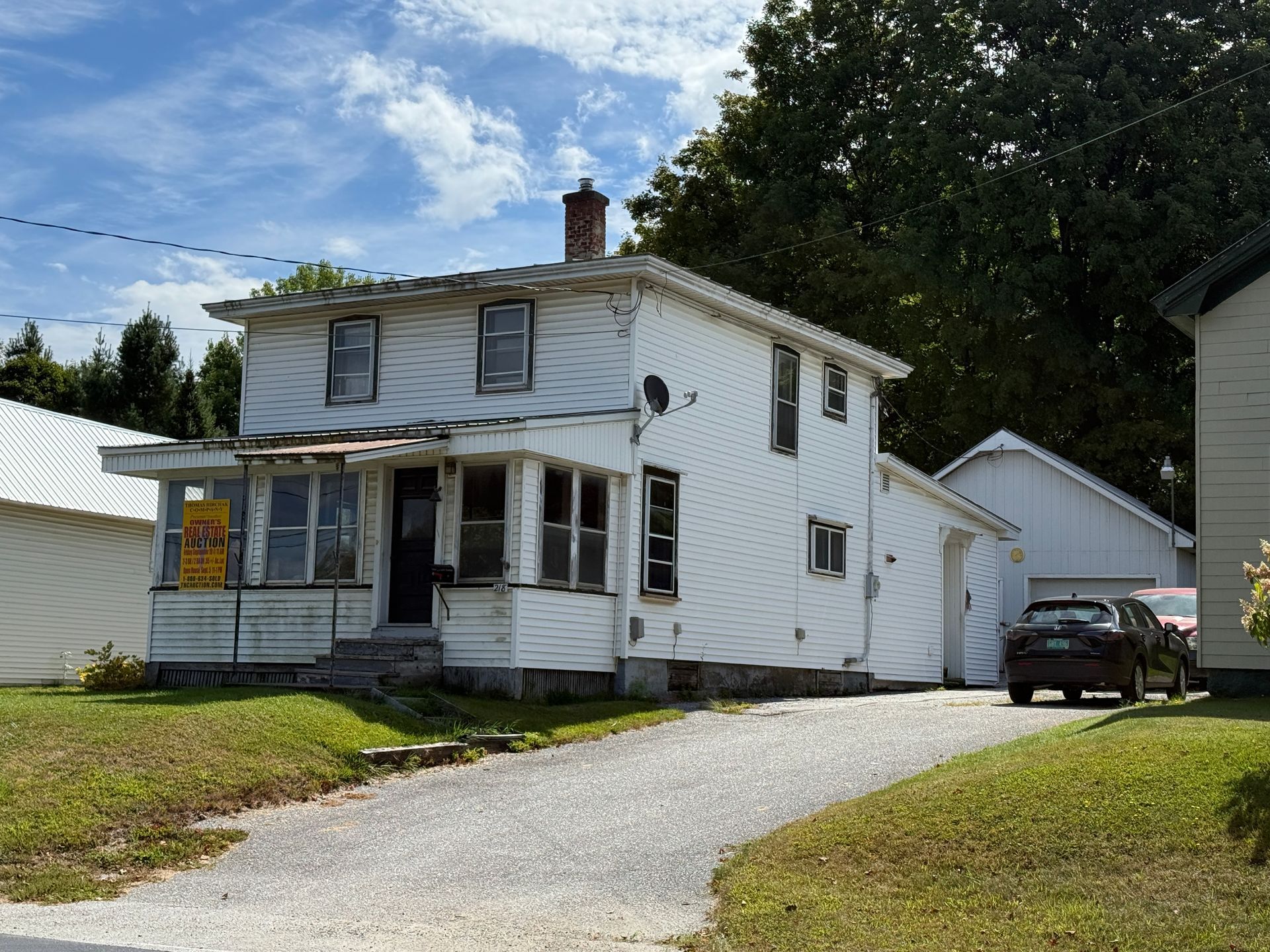 White two-story house with detached garage and a car in the driveway on a sunny day.