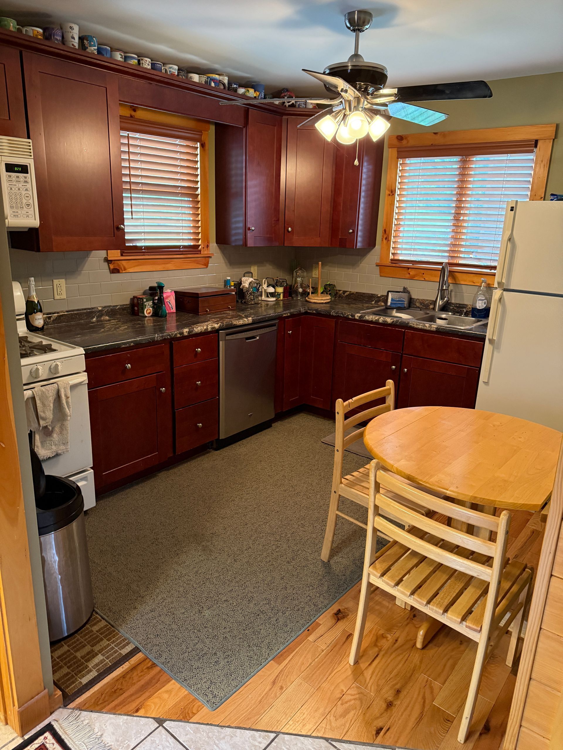 Kitchen with reddish-brown cabinets, gray countertops. Includes a table and chairs, and a stainless steel dishwasher.
