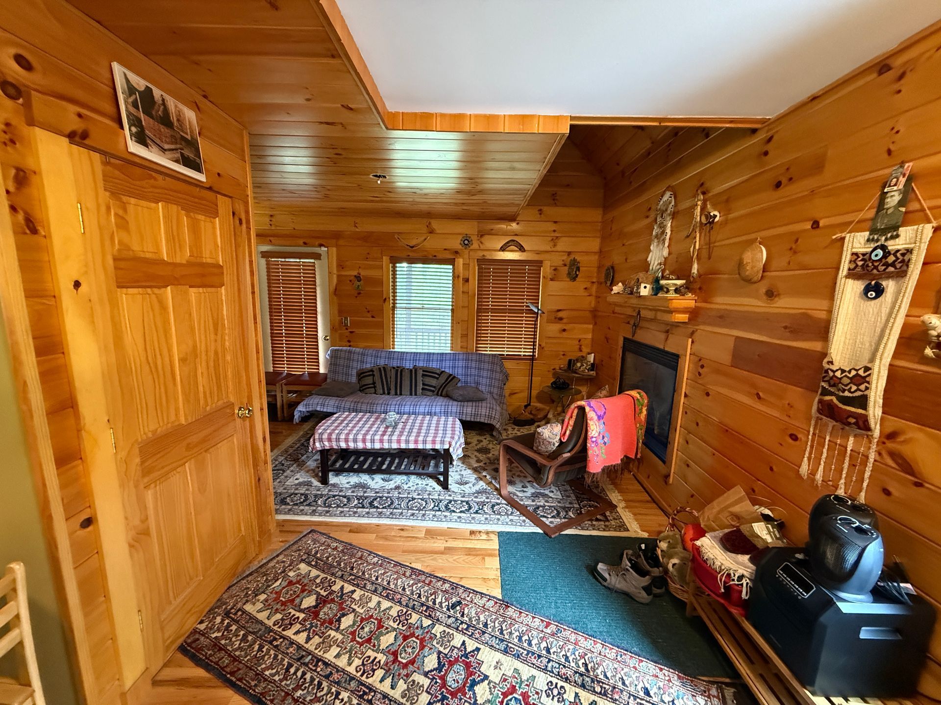 Wooden cabin interior with a fireplace, sofa, and rugs.