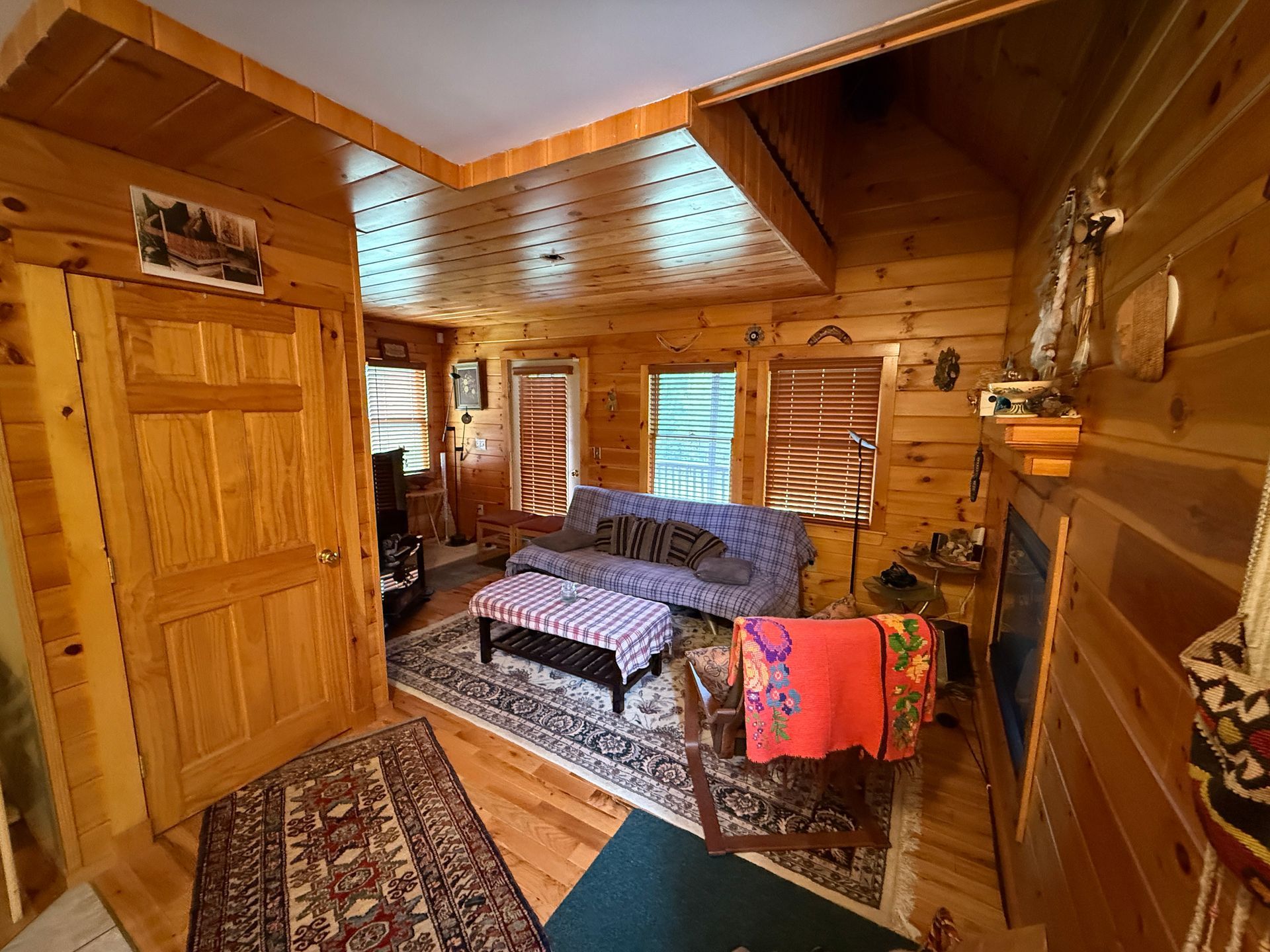 Cozy, wood-paneled cabin interior with sofa, rug, and small fireplace; warm tones.
