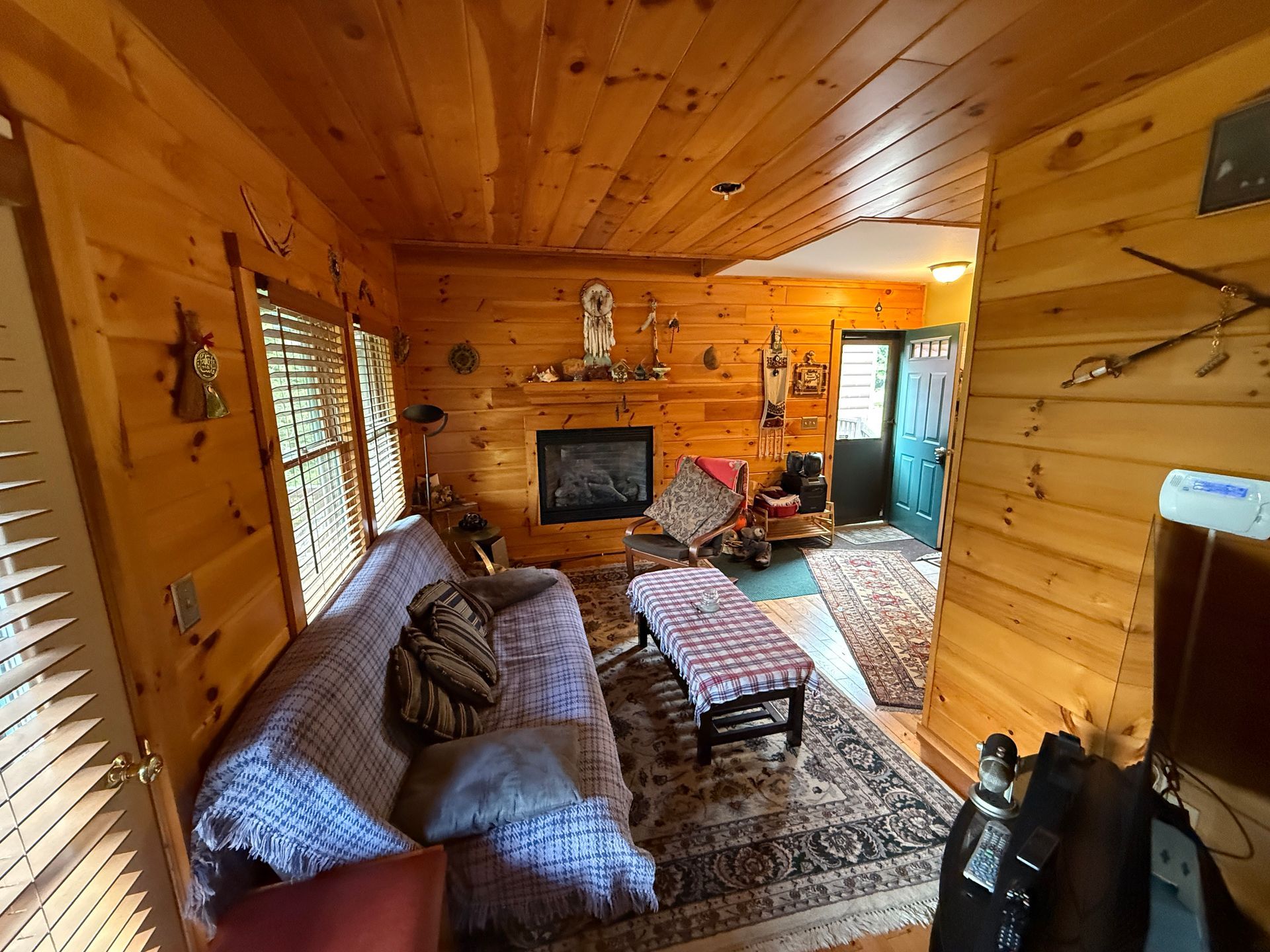Cozy cabin interior with wooden walls, fireplace, sofa, and rug. Entrance door visible.