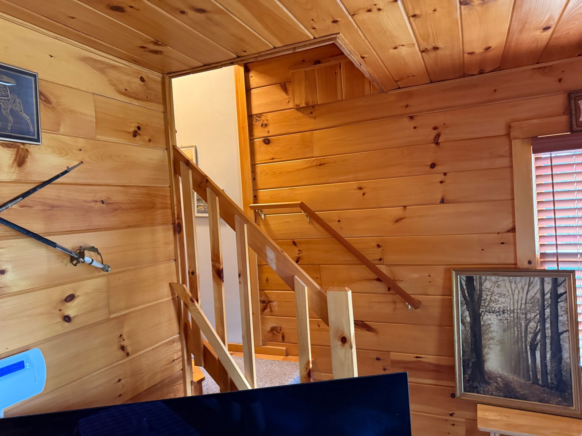 Wooden staircase set in a wood-paneled room.  A landscape picture and a window with blinds are visible.