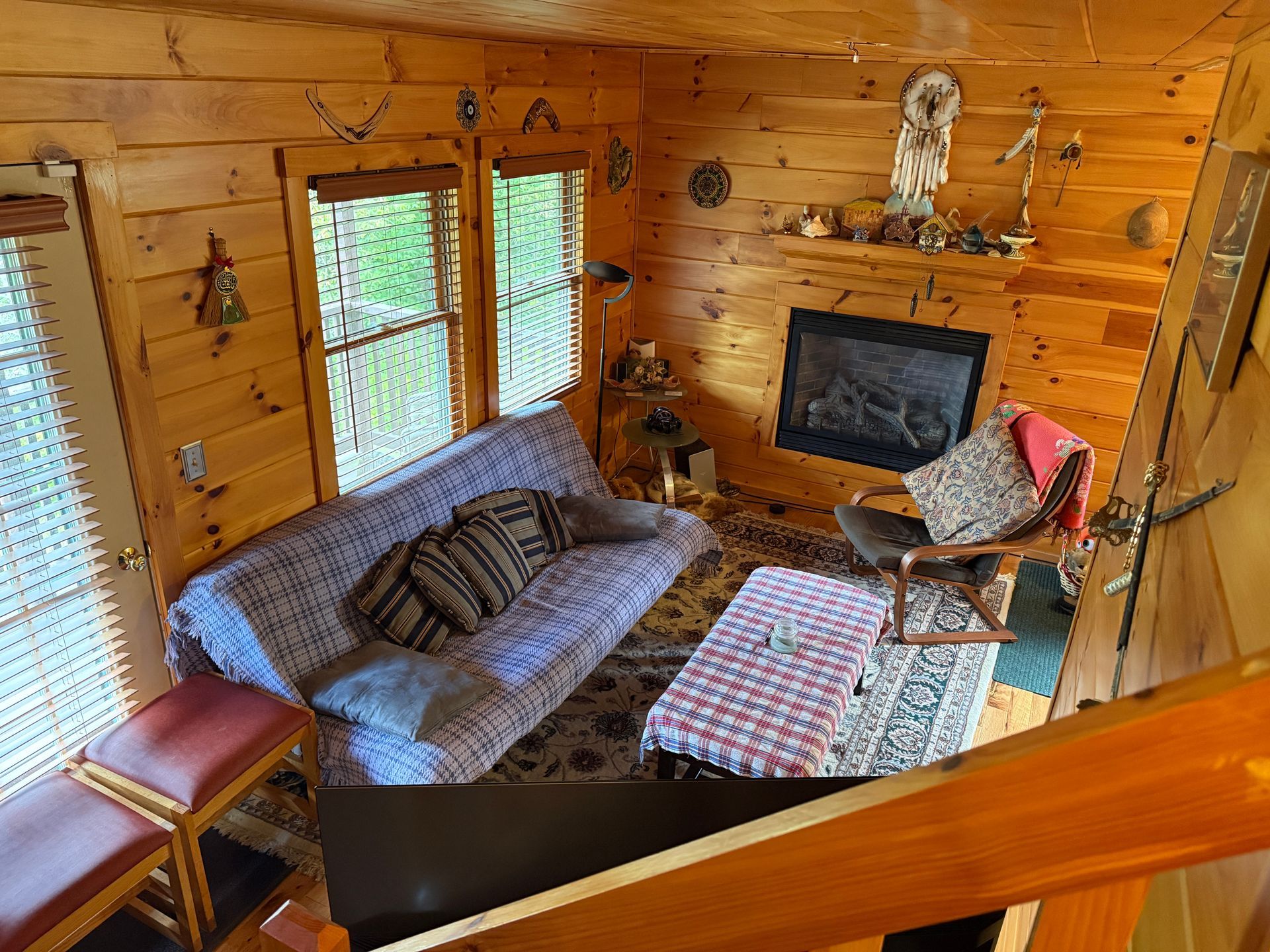 Cozy cabin living room with sofa, fireplace, windows, and wood paneling.