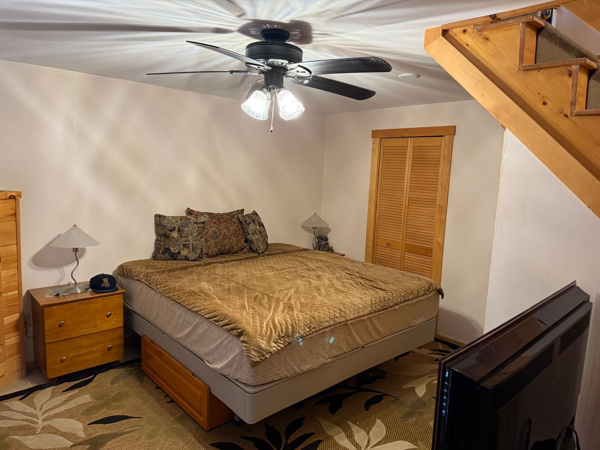 Bedroom with bed, dresser, TV, wooden door, and stairs. Ceiling fan.