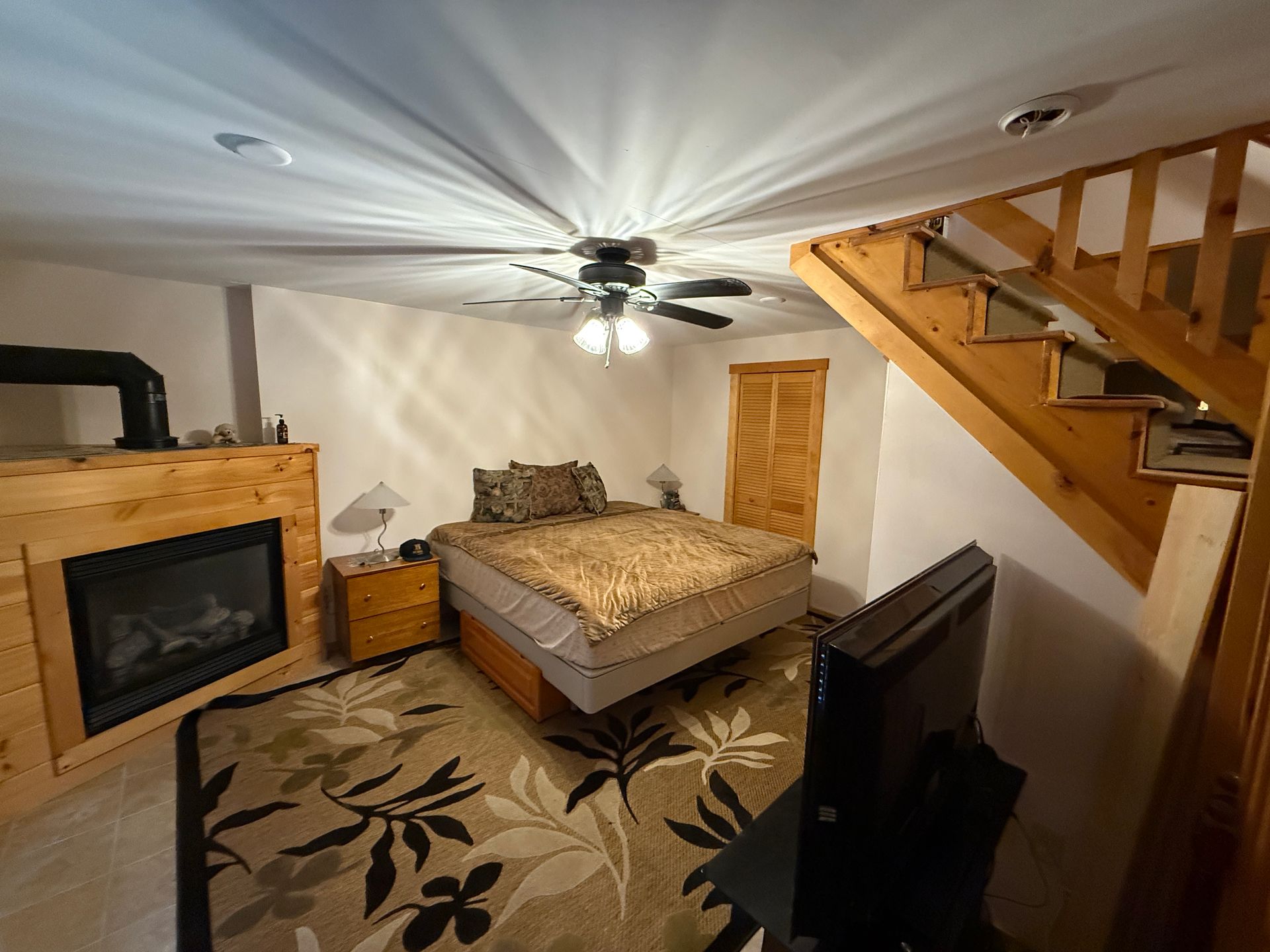 Bedroom with fireplace, bed, stairs, and television. Carpet with floral design.