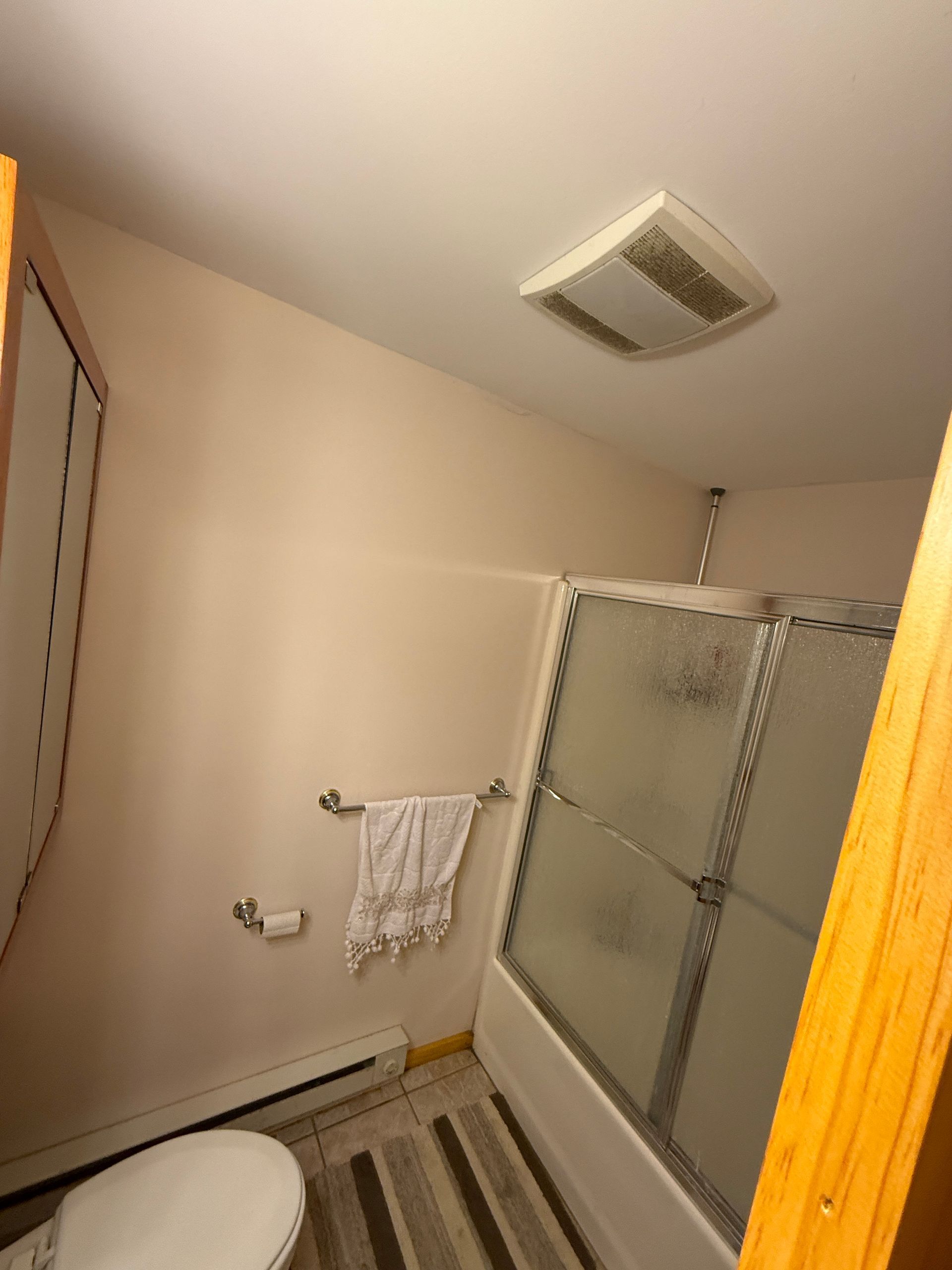 Bathroom interior with a shower, toilet, and towel rack; beige walls and ceiling.