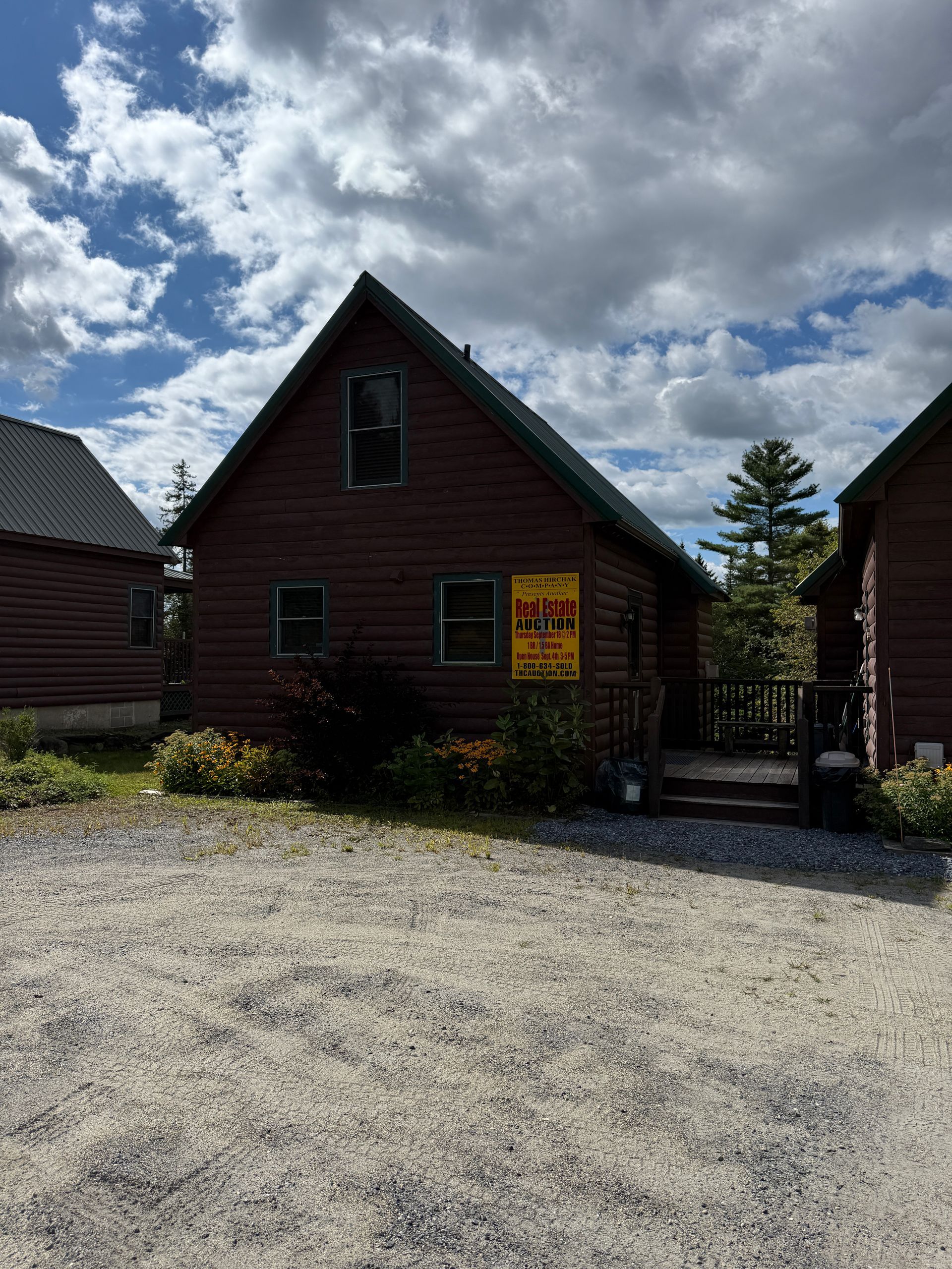 Brown cabin with a sign, surrounded by gravel and other cabins under a cloudy sky.