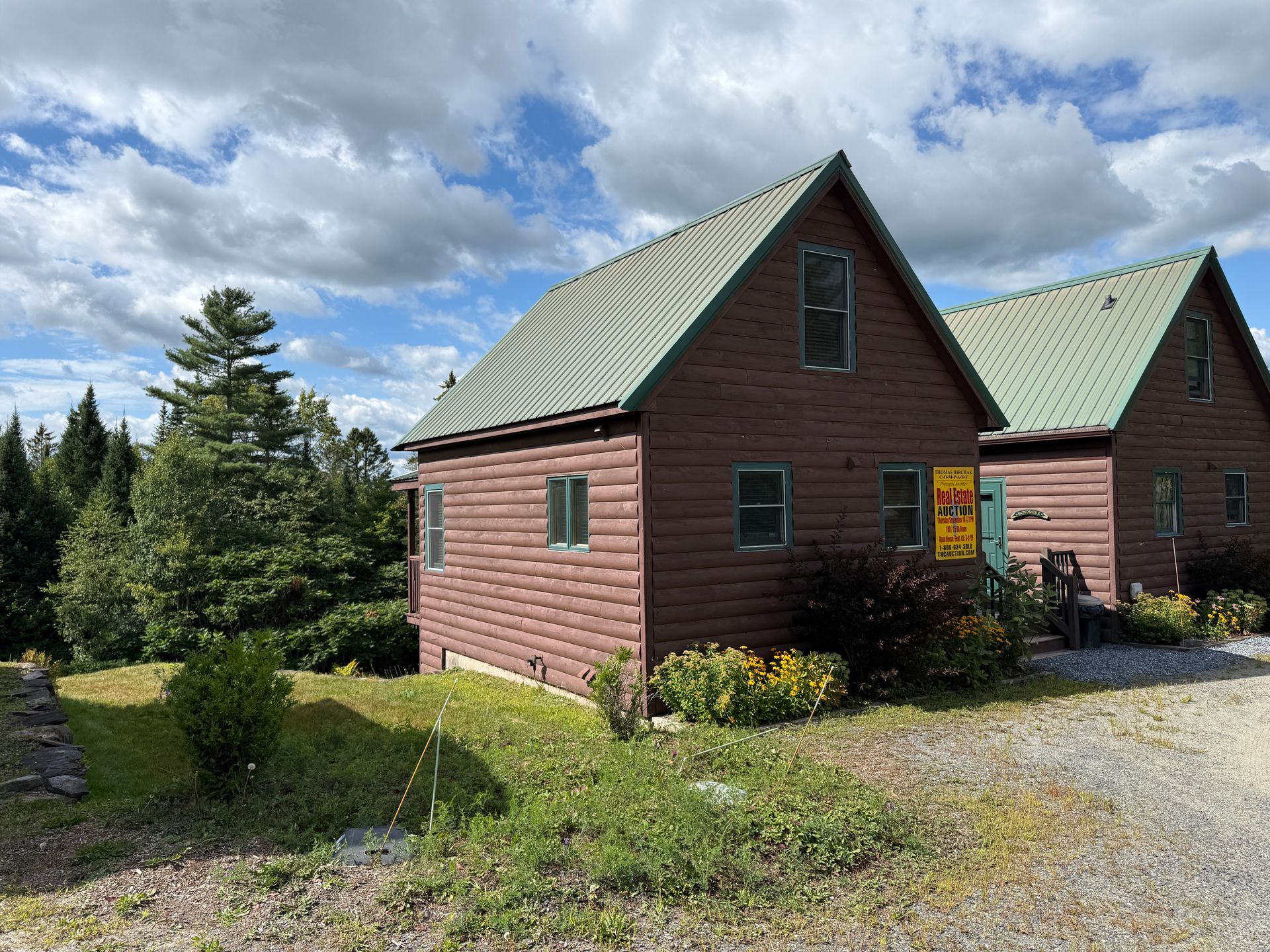 Two brown cabins with green roofs under a cloudy sky.