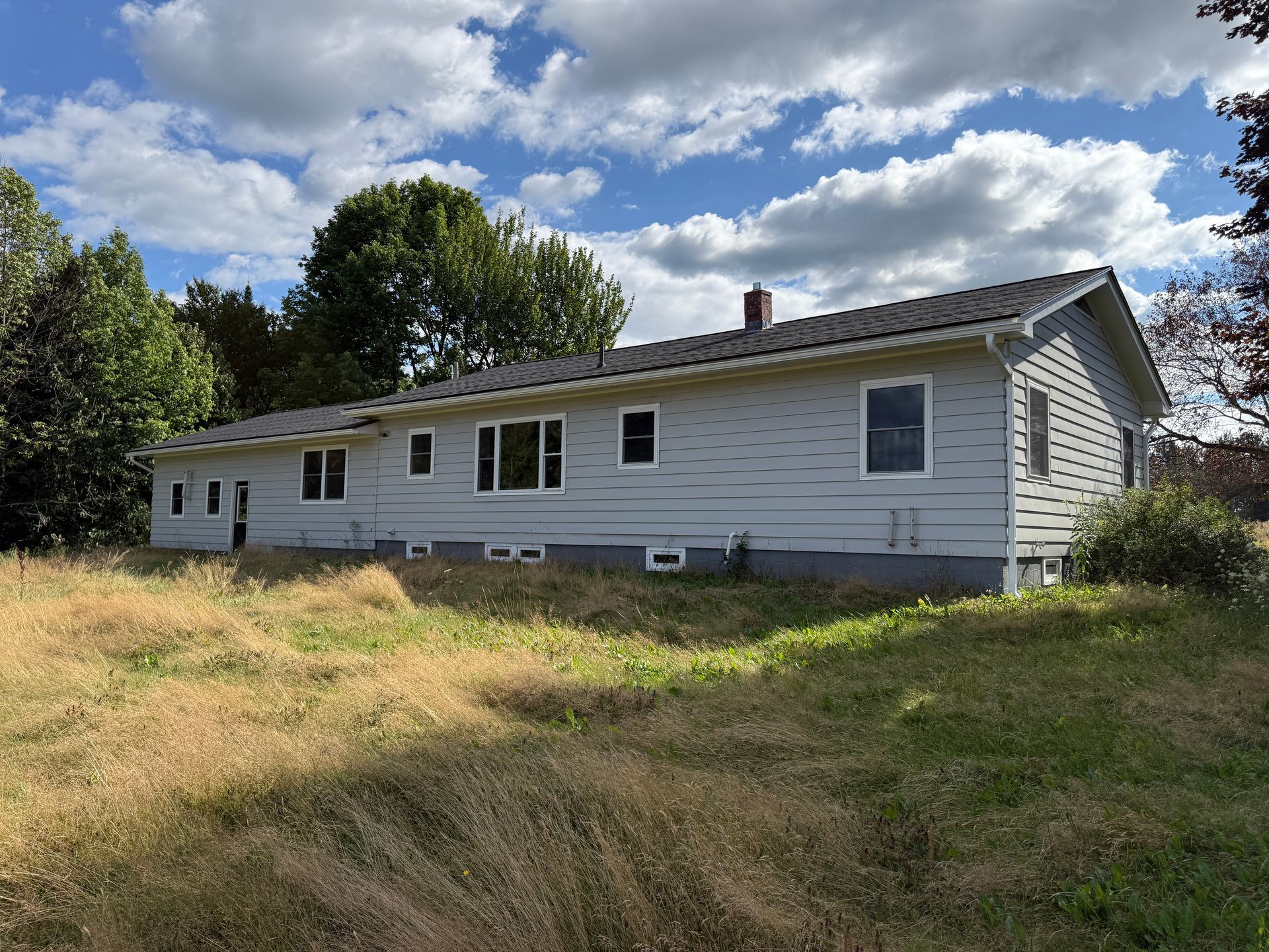 Side view of a light gray house with a yard under a cloudy sky.