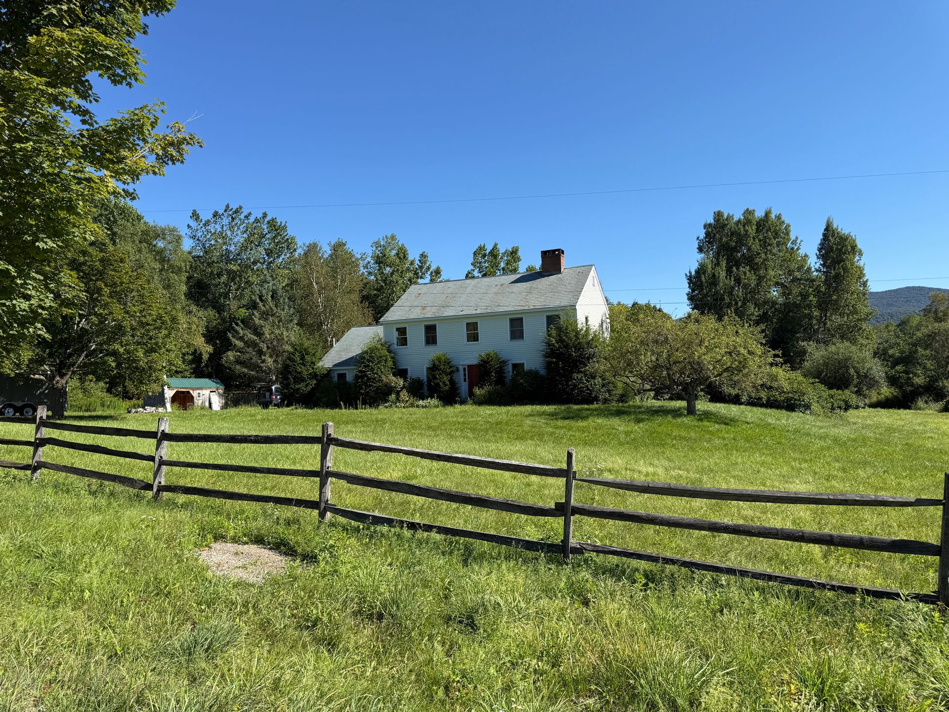 White farmhouse behind a wooden fence, in a grassy field on a sunny day.