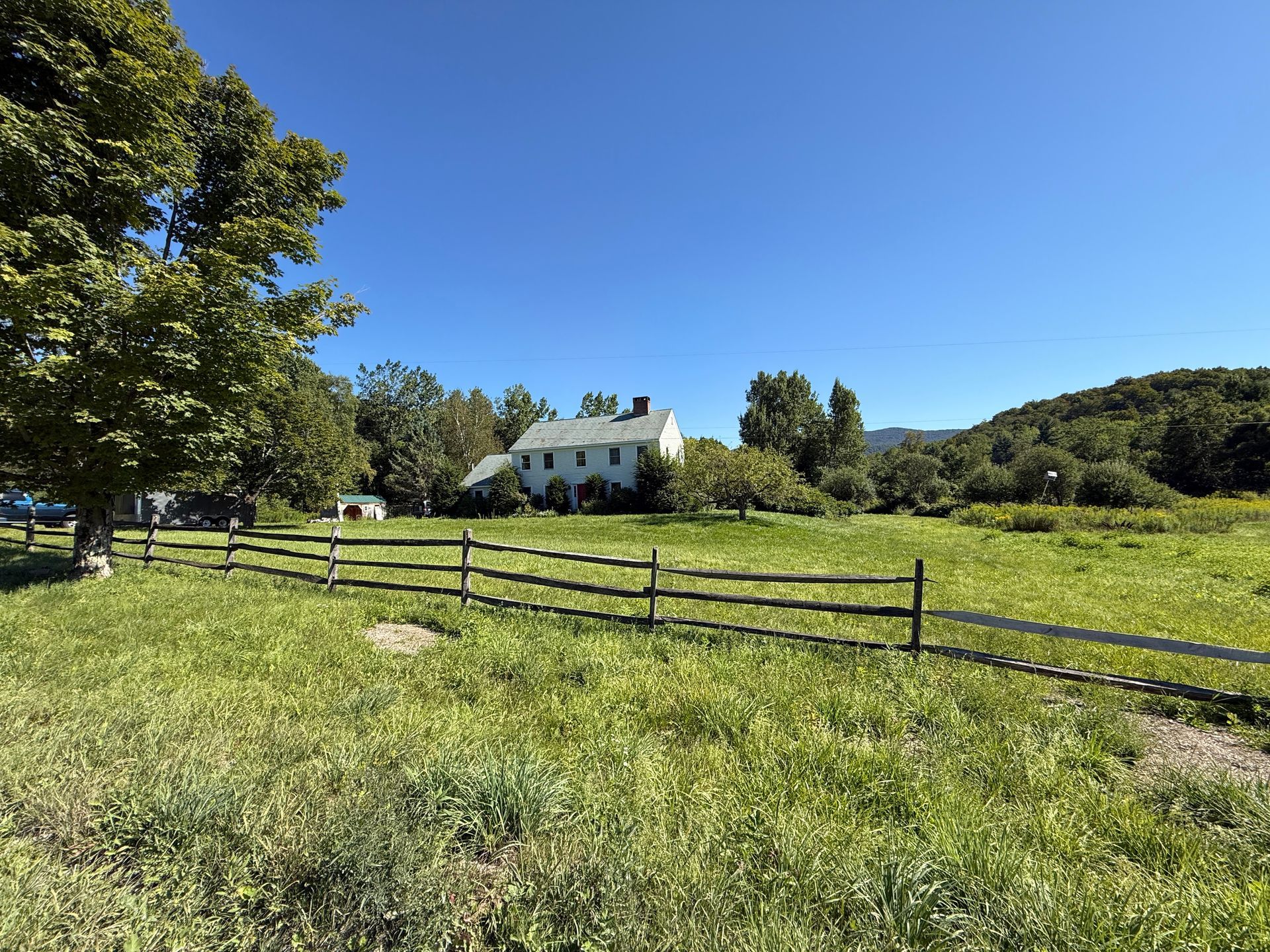 A white house in a sunny meadow with a wooden fence under a clear blue sky.
