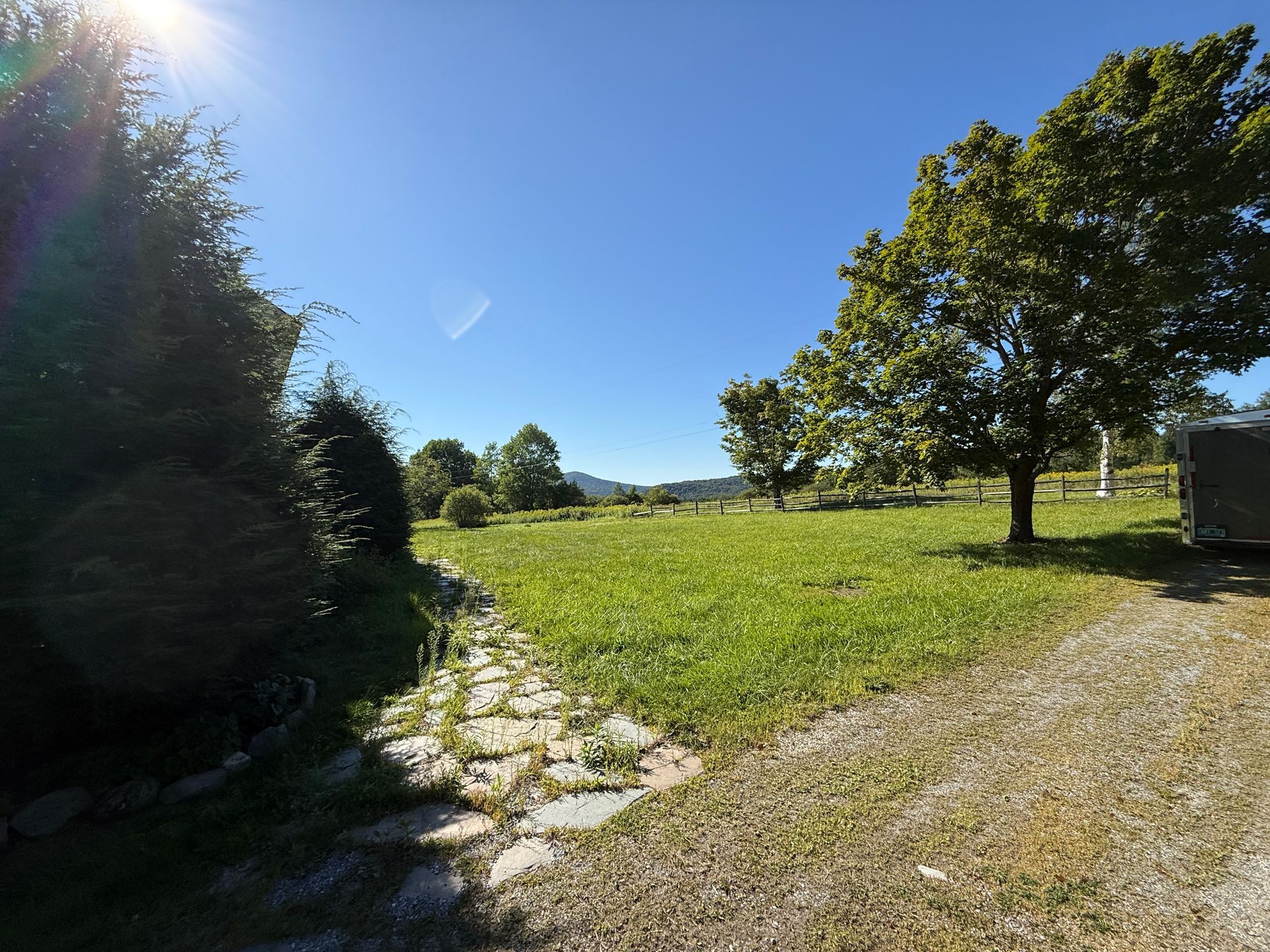 Bright sunny day in a grassy field with trees. A stone path leads to the field.