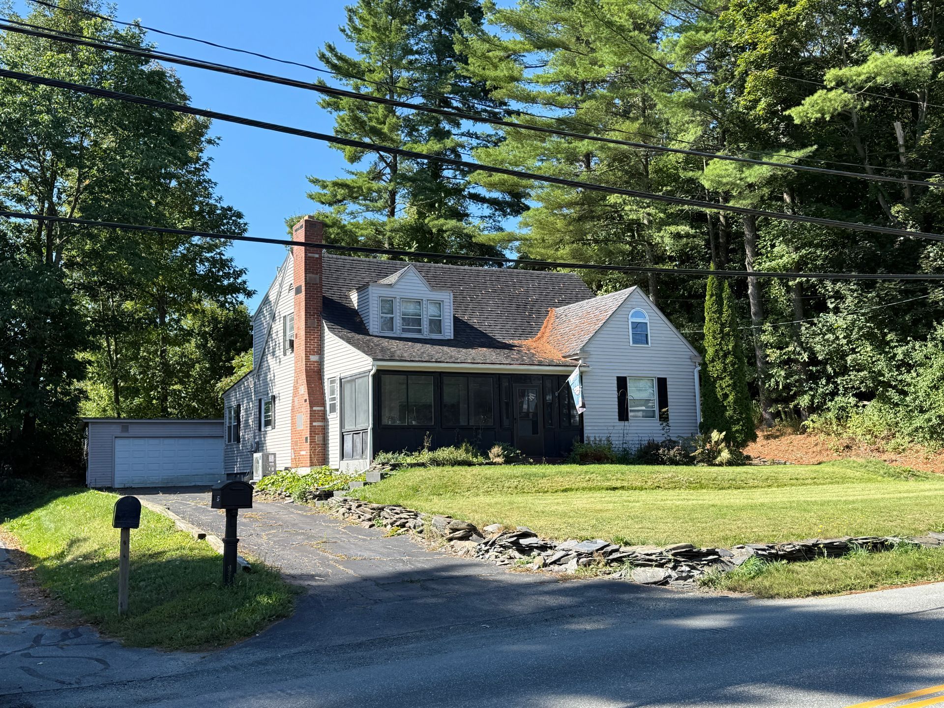 Cottage-style house with green lawn, driveway, and detached garage. Trees in the background, blue sky.
