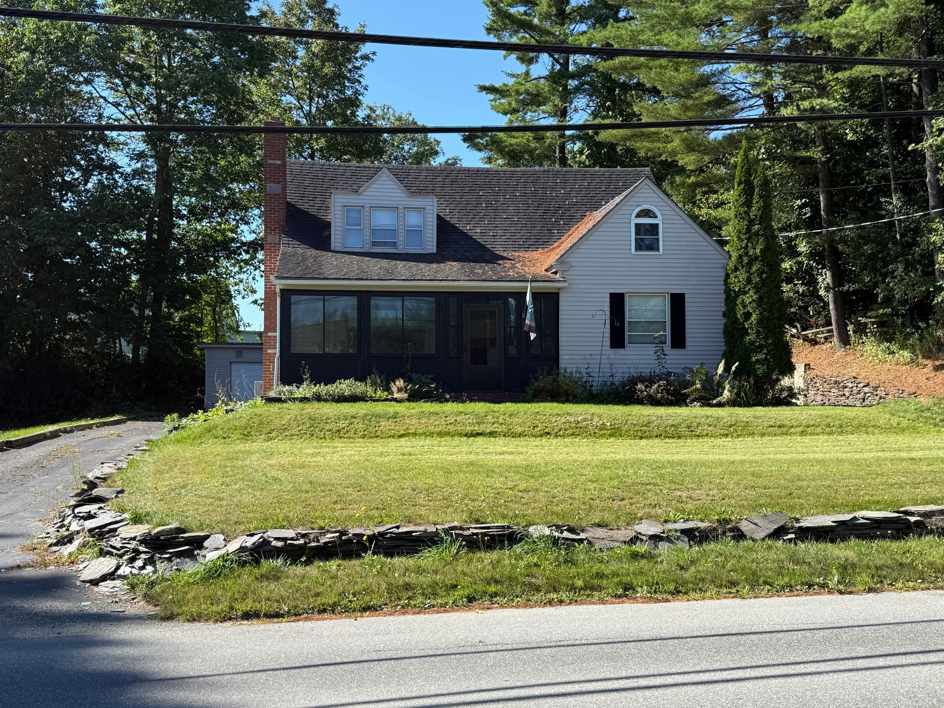 House with gray siding, dormers, and a chimney, set in front of a grassy lawn on a sunny day.