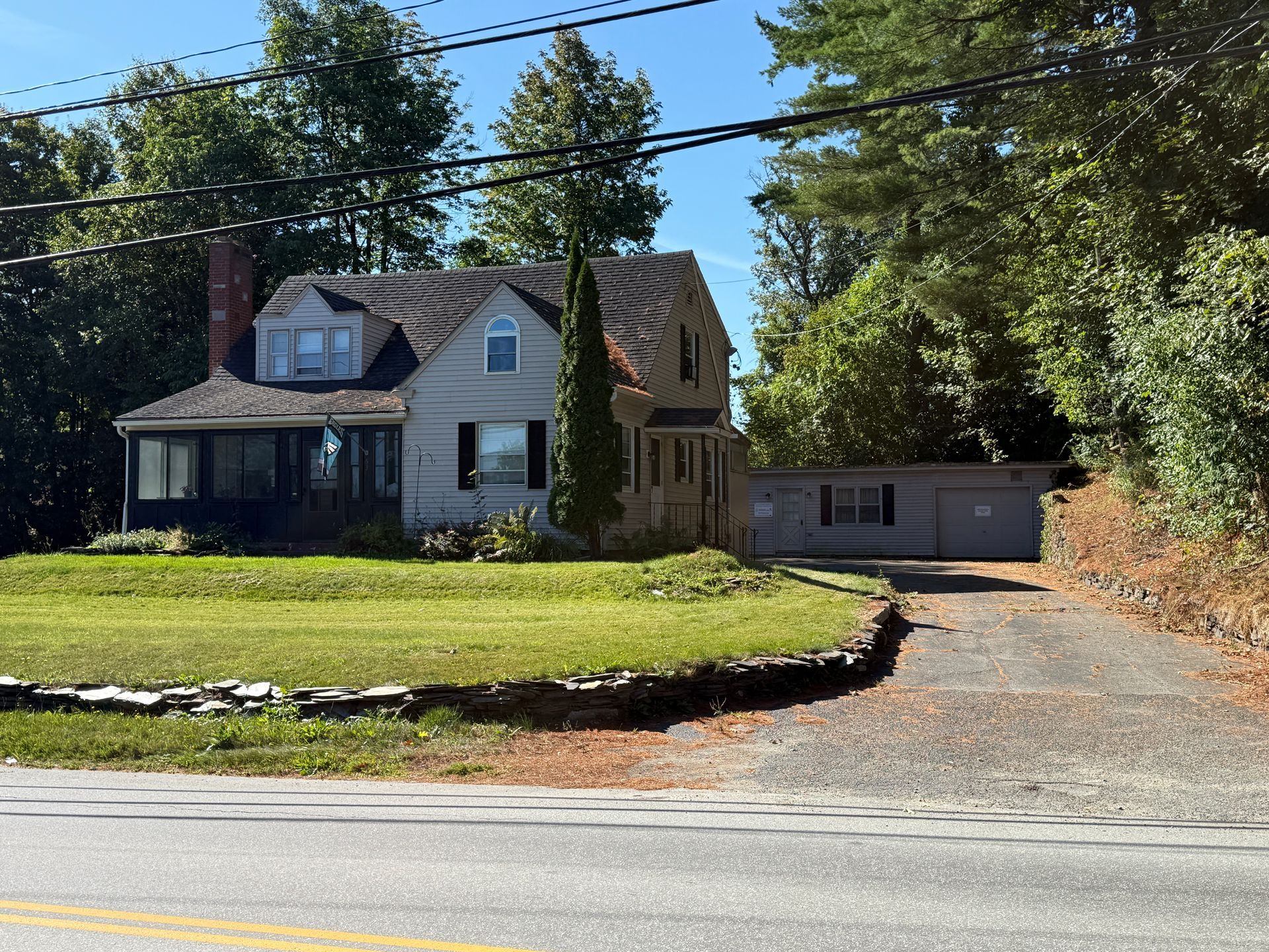 House with a gray exterior, black shutters, and a sloped roof, with a driveway and green lawn.