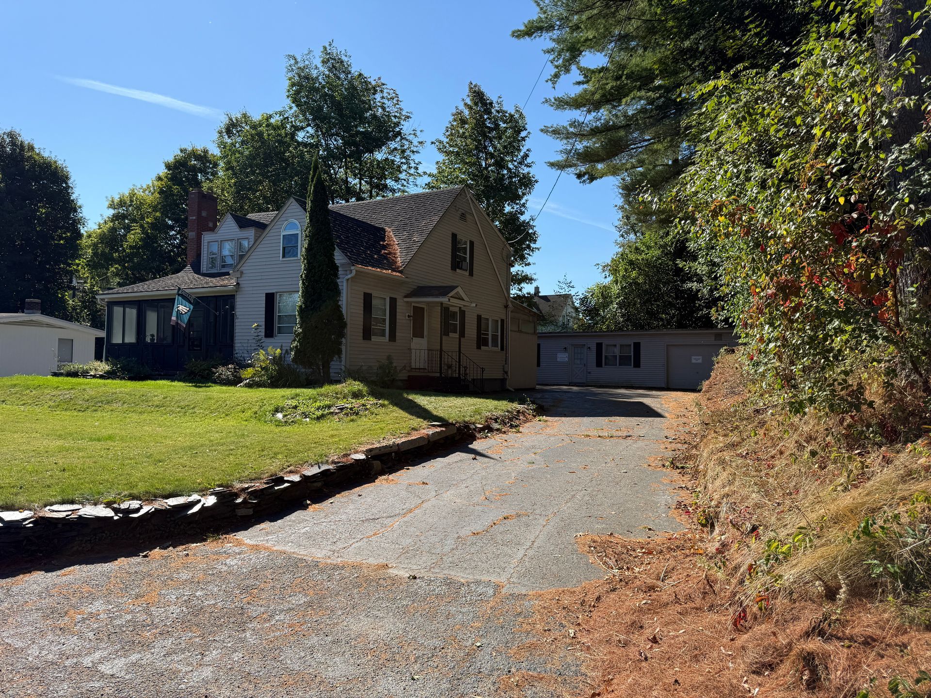 Gravel driveway leads to a two-story house with green lawn on a sunny day.