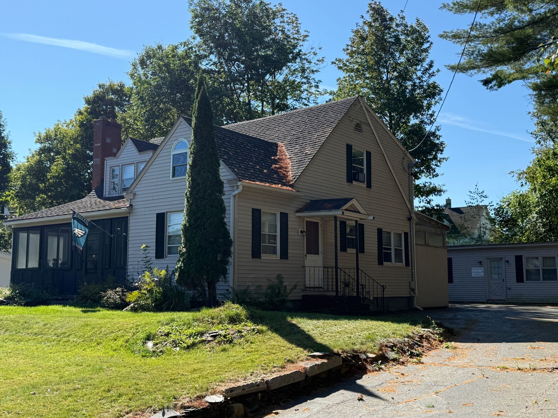 Beige two-story house with black shutters, porch, and a lawn with trees.