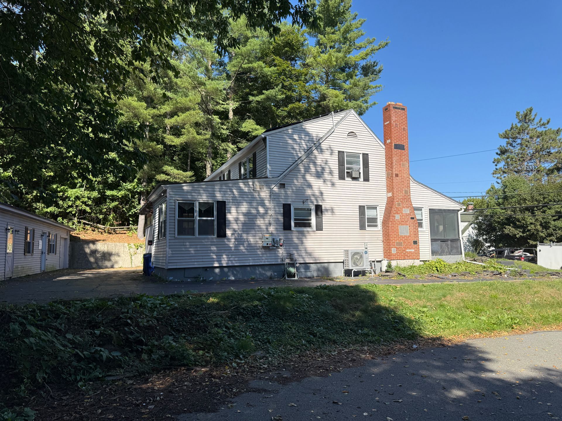 A two-story white house with a red brick chimney and a grassy yard under a blue sky.