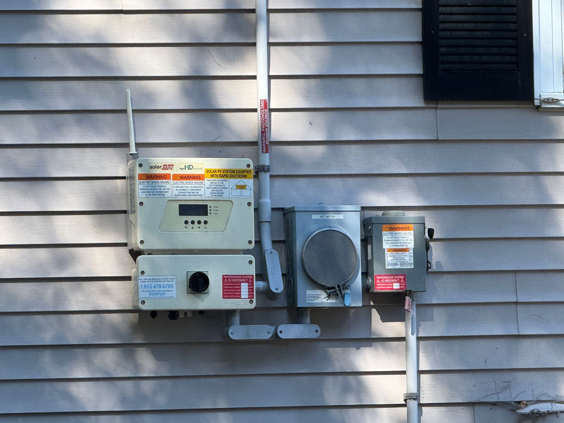 Electrical components mounted on a house's siding: inverter, meter, and breaker box.