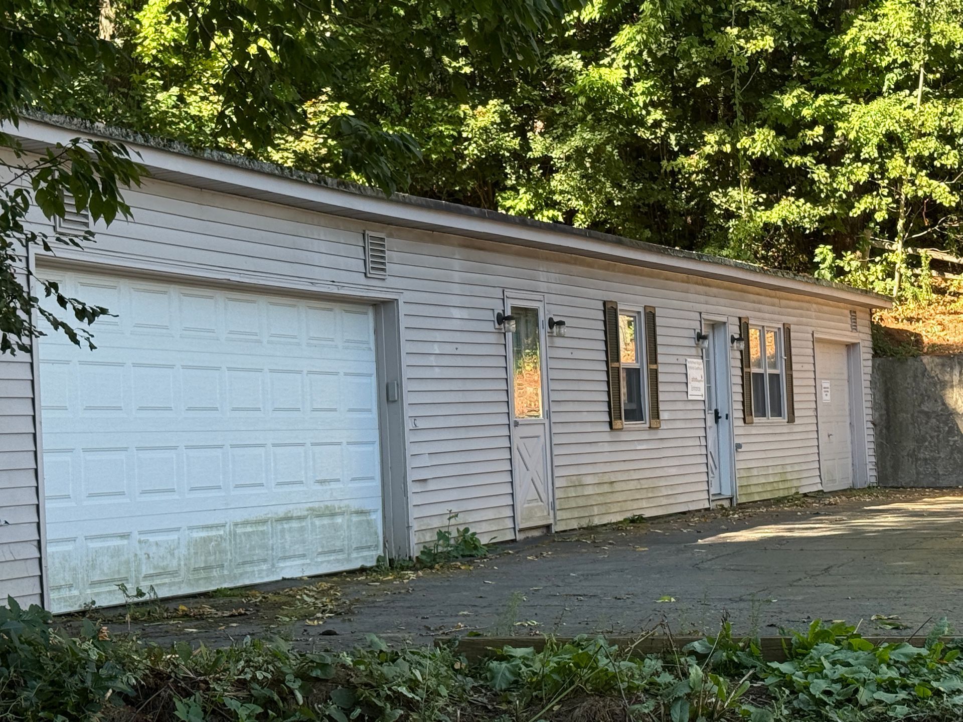 Light-colored garage with multiple doors and windows, set against a backdrop of green trees.