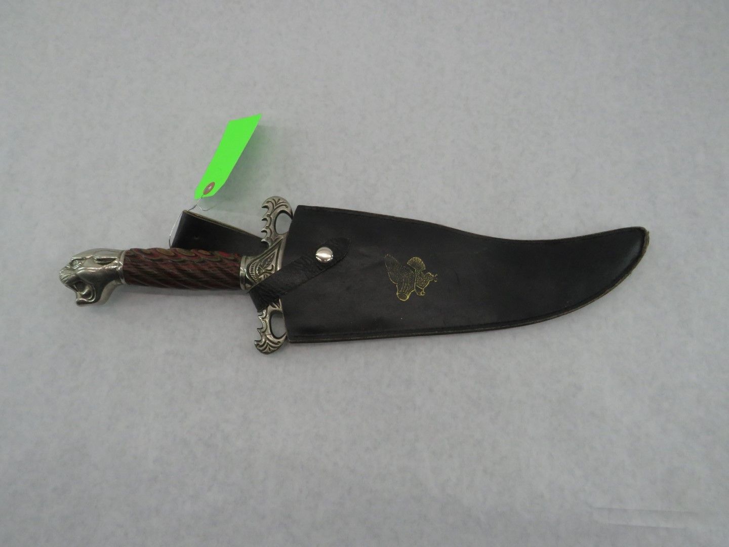 Knife in a leather sheath with a decorative handle, resting on a white surface.