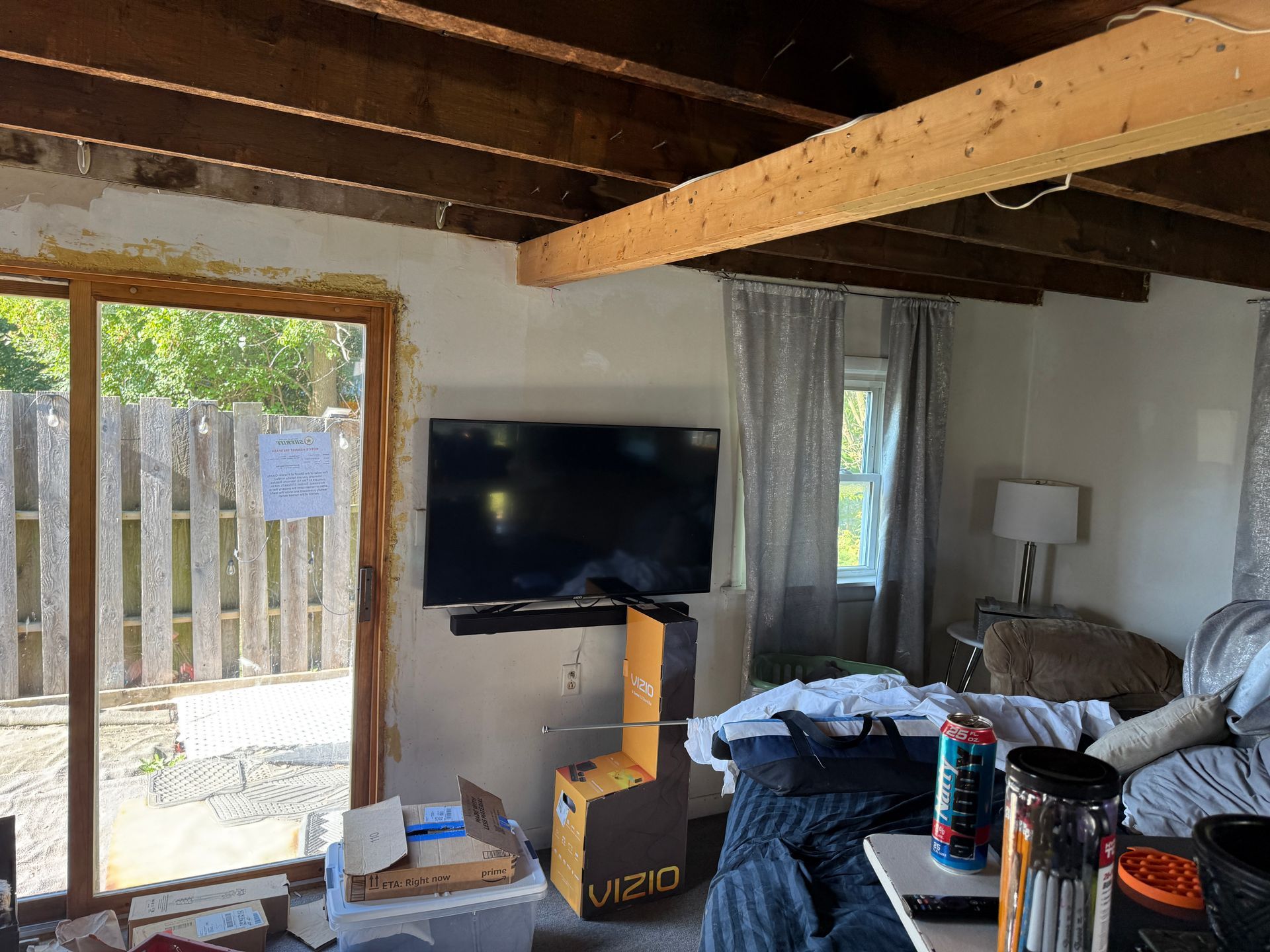 Interior of a room with a mounted TV, sliding glass door, exposed wooden beams, and furniture.