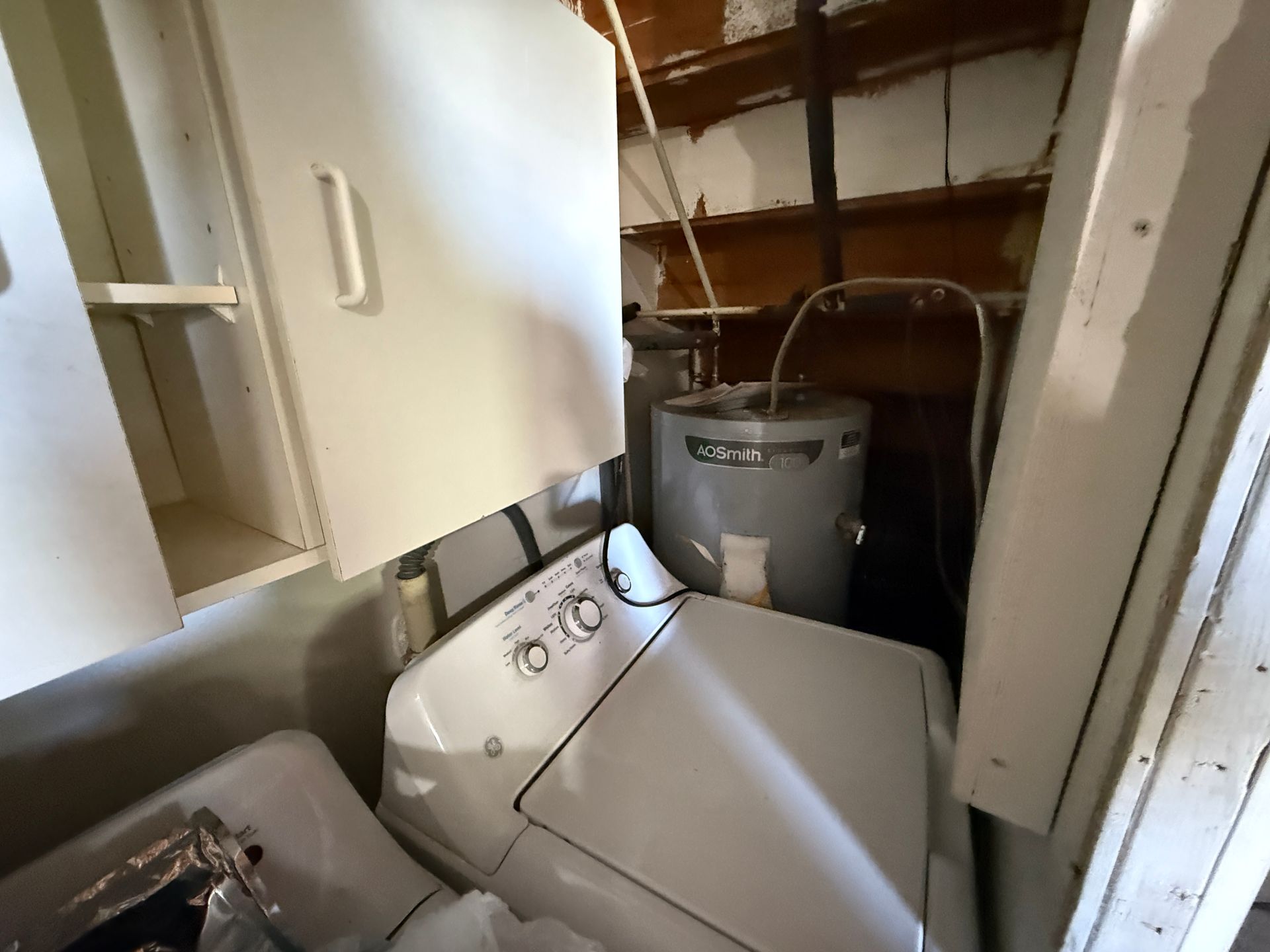 Laundry room with washer, dryer, water heater, and cabinets. White appliances and storage against walls.