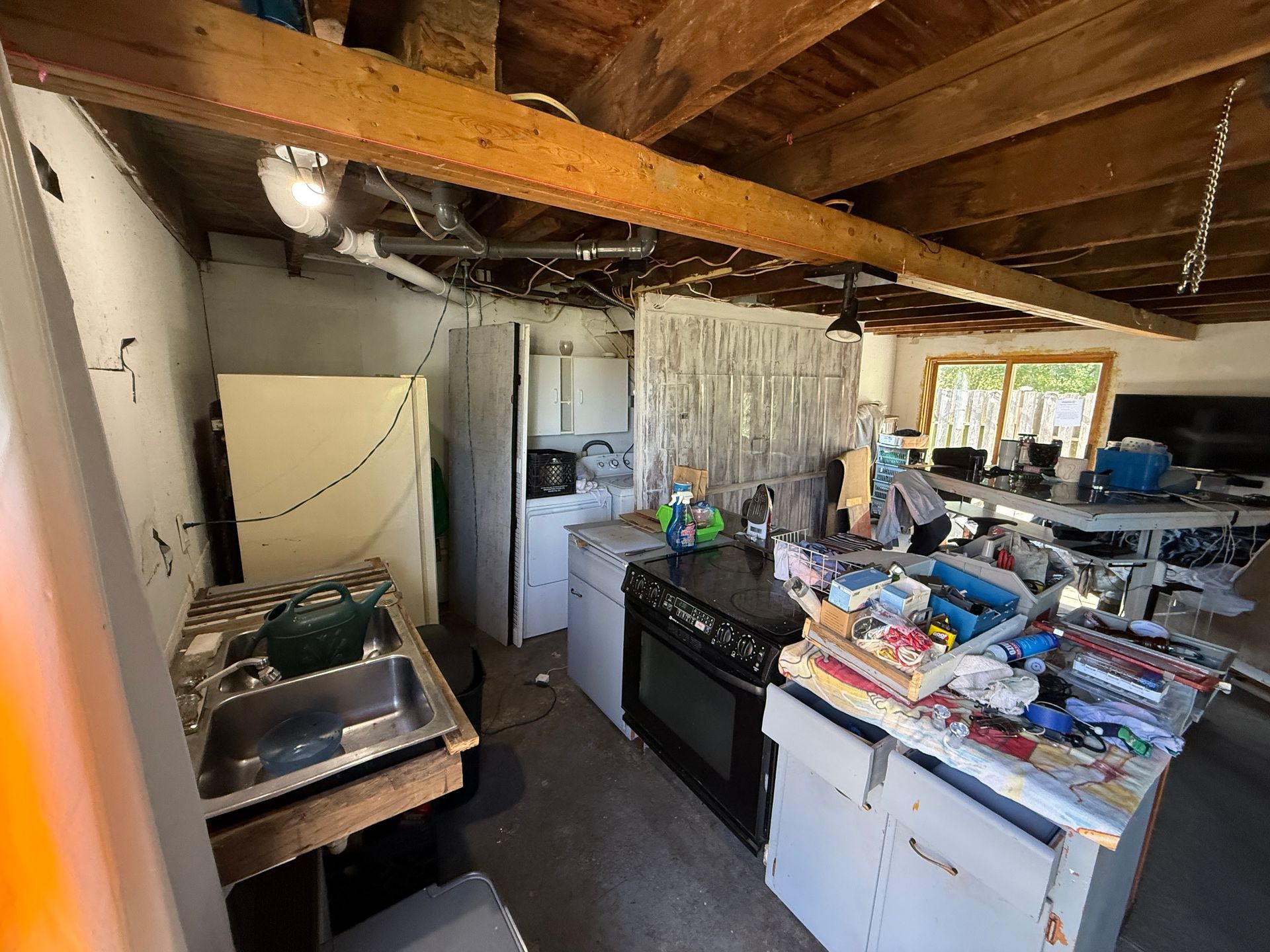 Kitchen with appliances, including a refrigerator, stove, and sink. Unfinished ceiling and shelves.