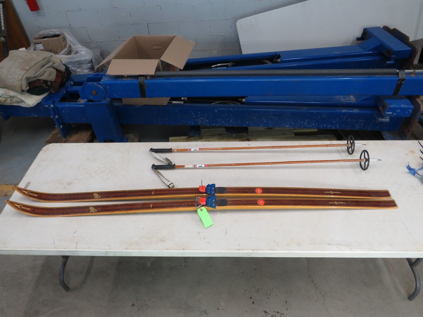 Wooden skis and poles on a white table. Blue binding, black and brown accessories.