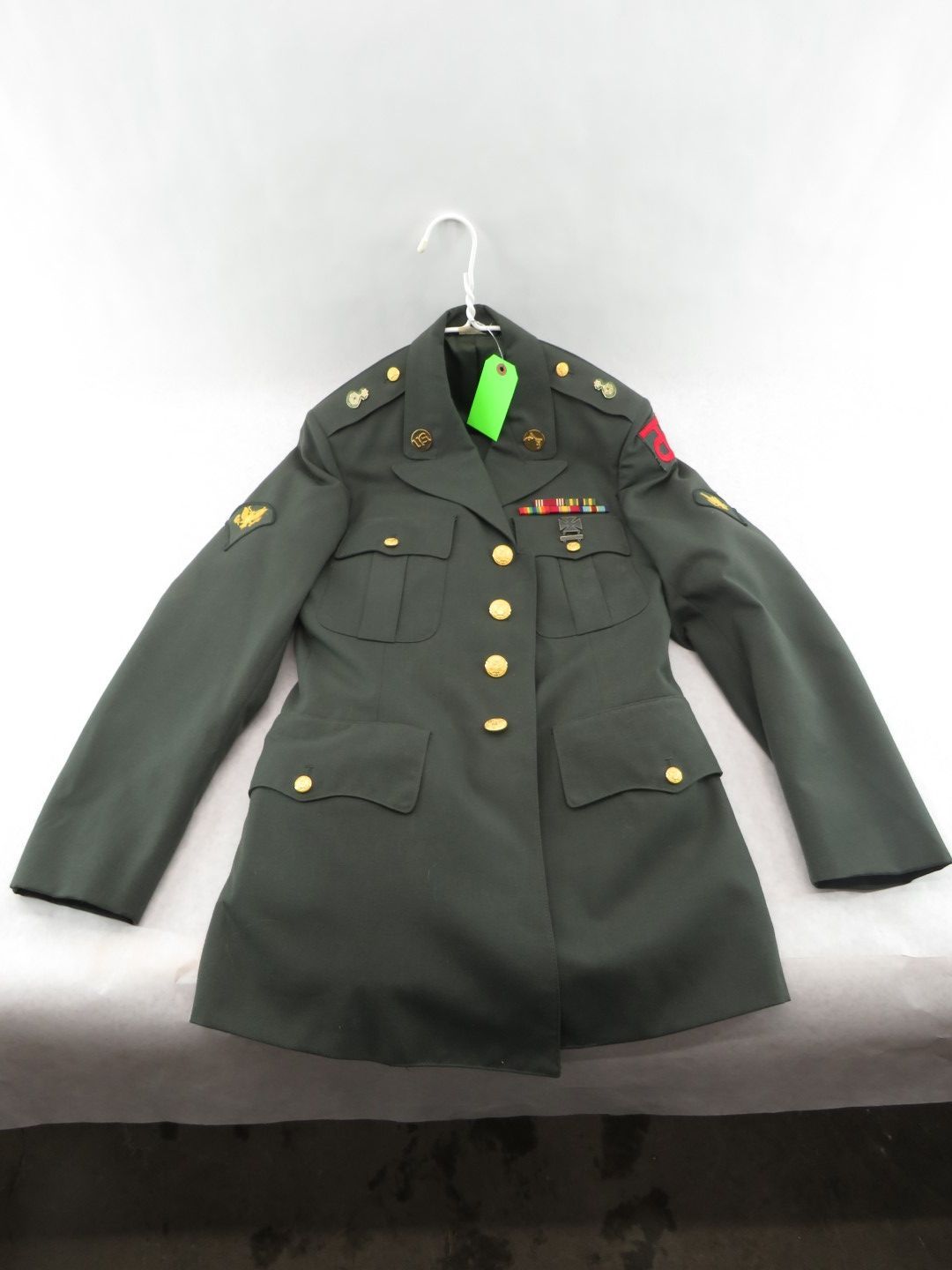 Green military uniform jacket on a hanger; gold buttons, insignia, and ribbons.