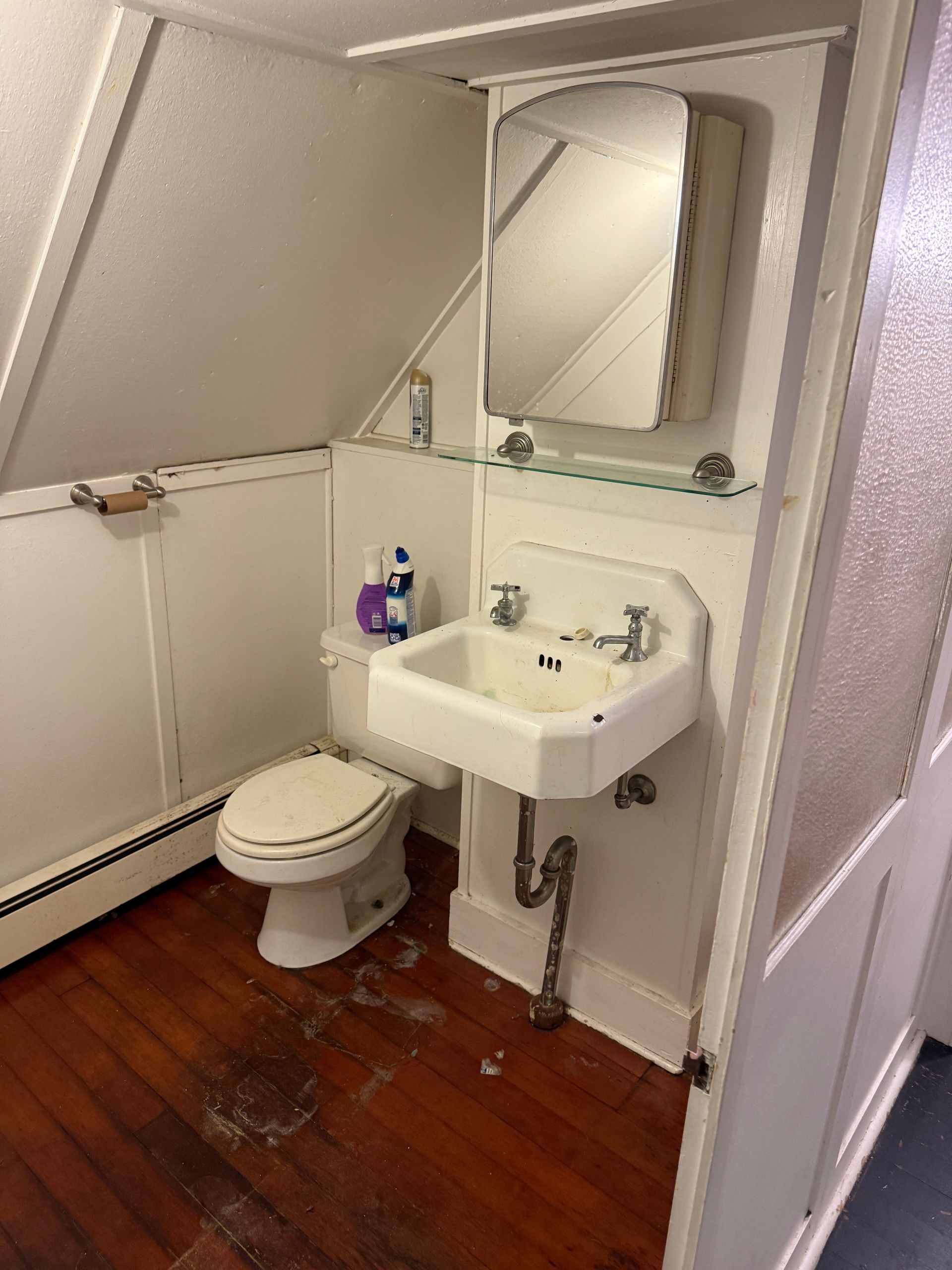 Small bathroom with a toilet, sink, and medicine cabinet; white walls, brown wood floor.