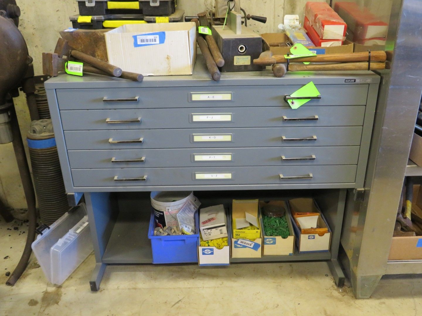 Gray metal cabinet with multiple drawers and an open shelf, tools on top and below.