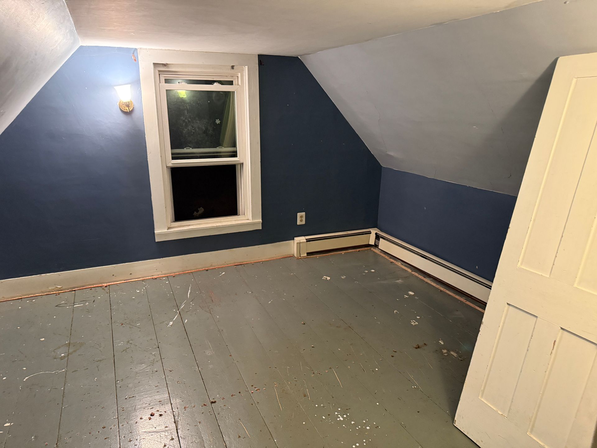 Empty room with blue walls and a window. White door leaning against the wall. Gray floor.